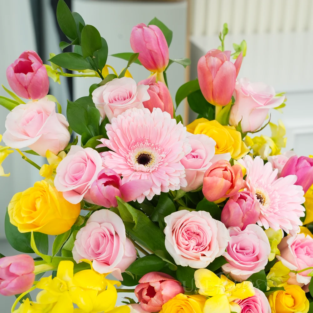 A basket arrangement of 3 pink gerberas, 15 pink roses, 5 yellow roses, 10 pink tulips and 5 stems of yellow orchids with green fillers and multi-colored easter eggs.