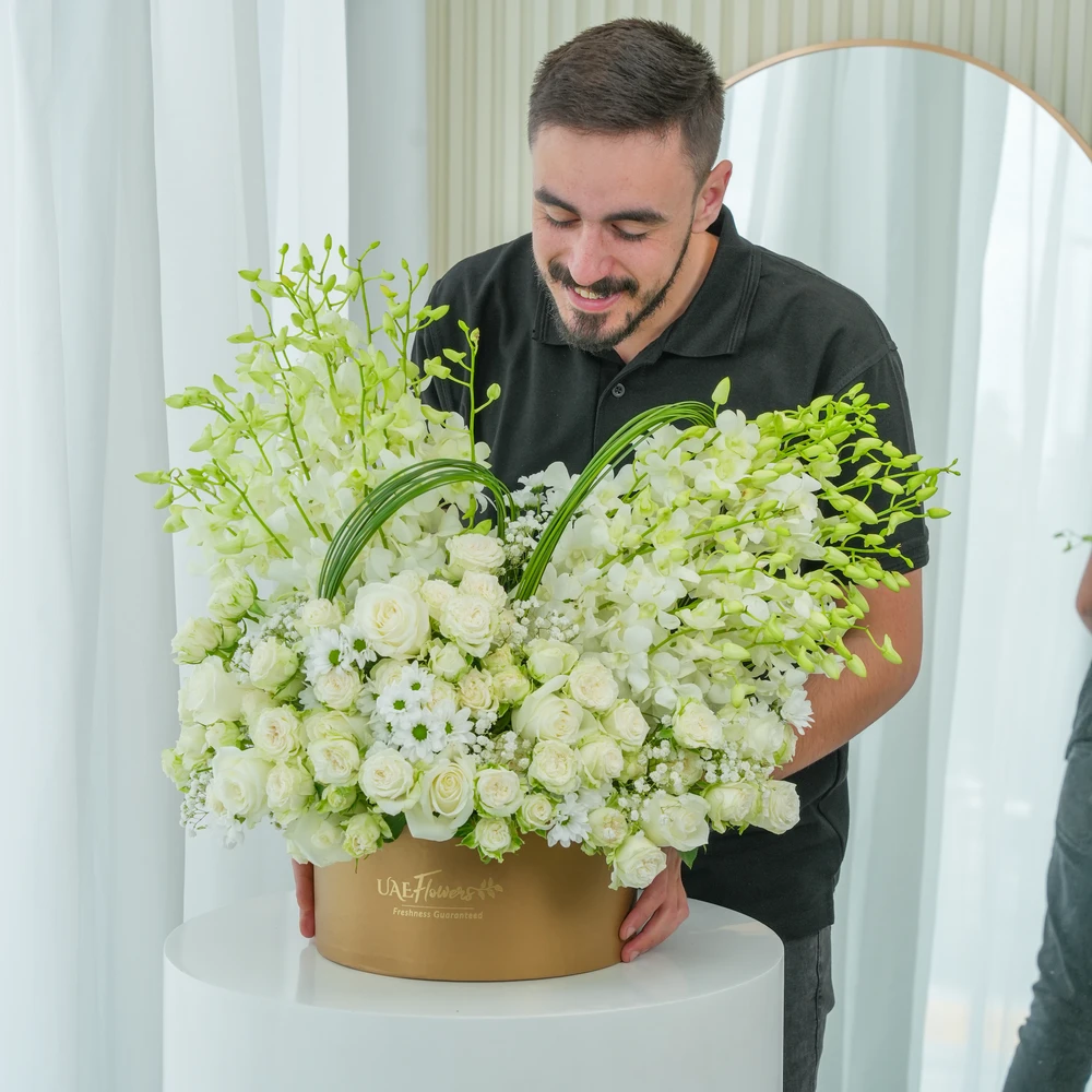 A box arrangement of 20 white orchids, 20 white roses, 5 white spray roses with white chrysanthemums and steel grass.