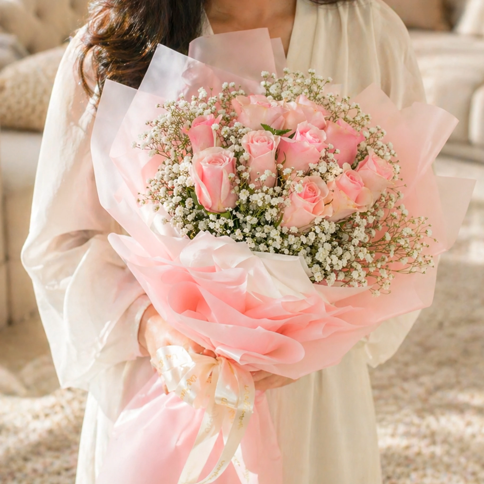 A bouquet of 10 pink roses with gypsophila and eucalyptus leaves in brown wrapping paper tied with pink ribbon