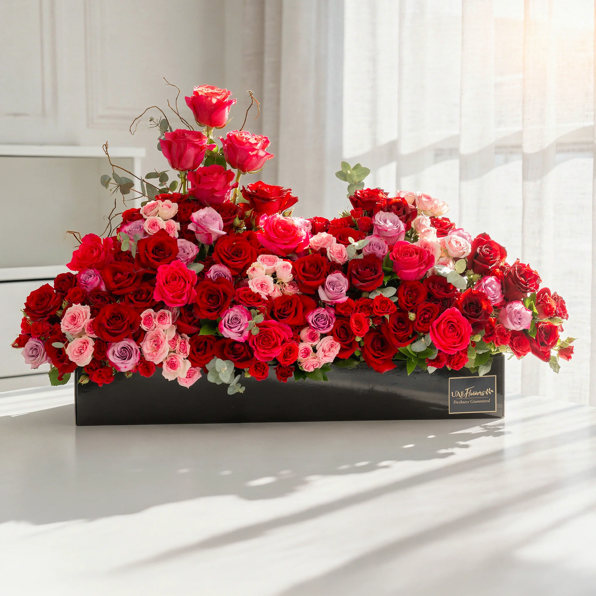 Arrangement of 20 red roses, 20 purple roses, 10 fuchsia roses, 20 red spray roses and 10 pink spray roses with green fillers in a long black box.
