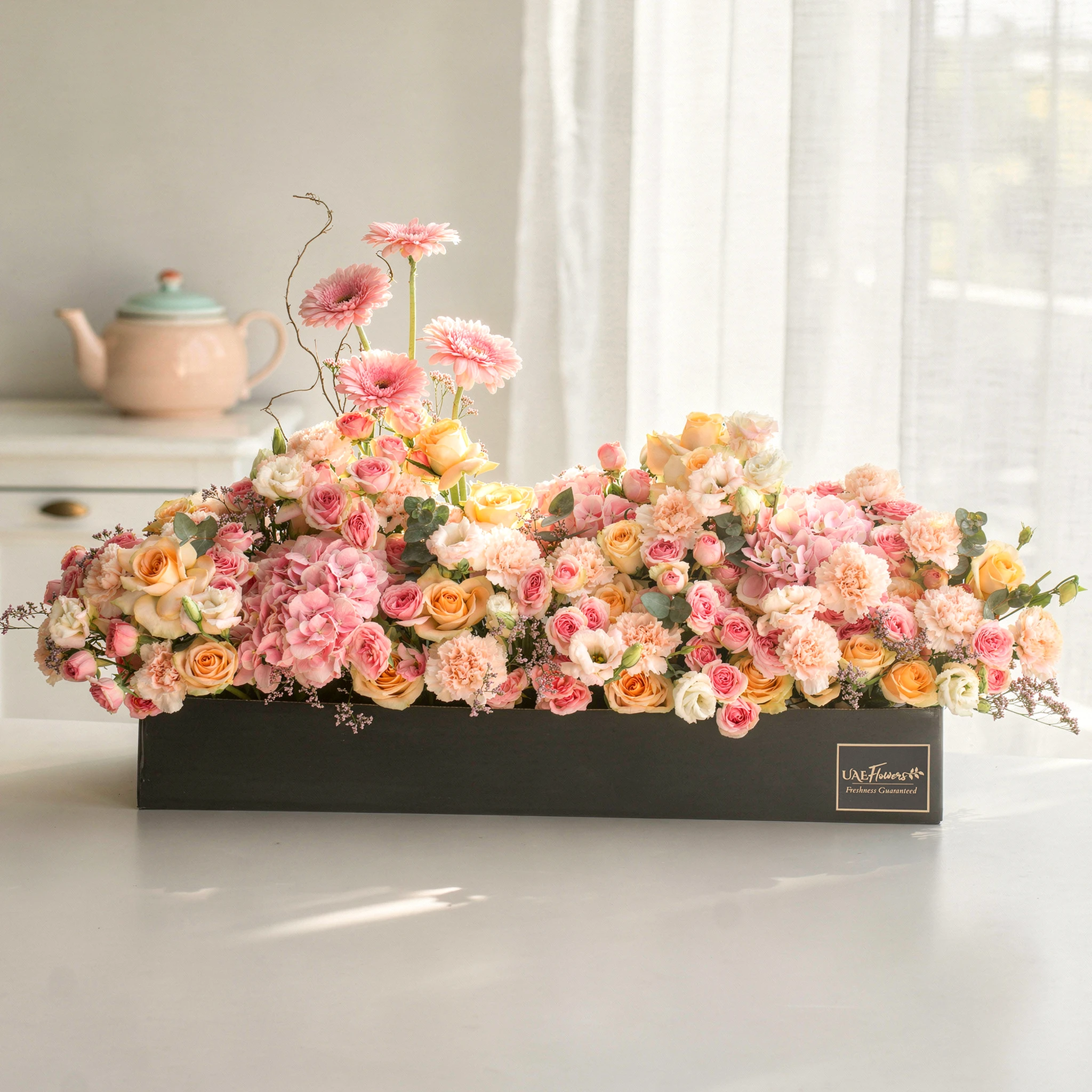 Arrangement of 4 pink gerberas, 3 pink hydrangeas, 20 pink carnations, 20 pink spray roses and 30 peach roses with green fillers in a long black box.