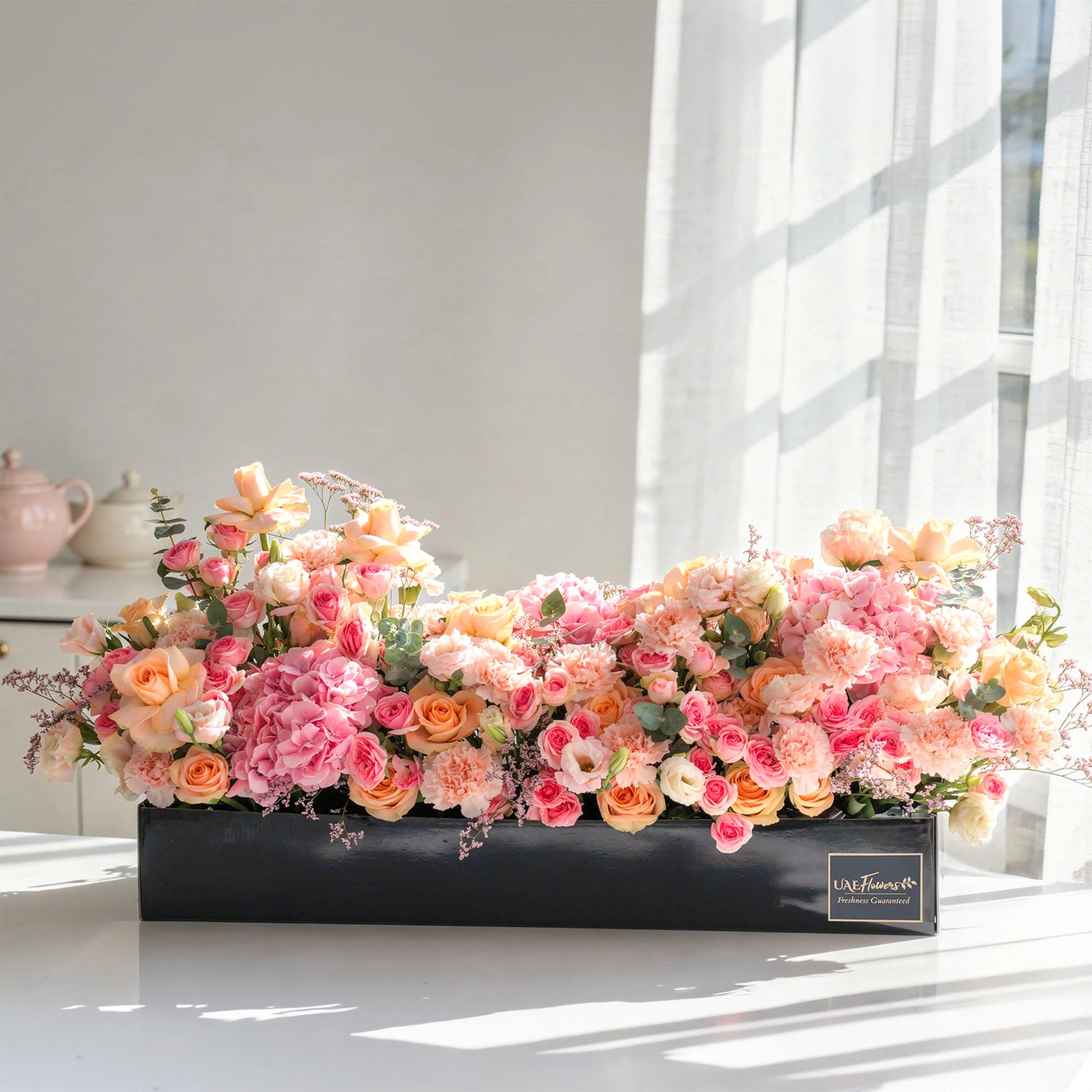 Arrangement of 20 peach roses, 20 pink carnations, 20 pink spray roses and 3 pink hydrangeas with green fillers in a long black box.