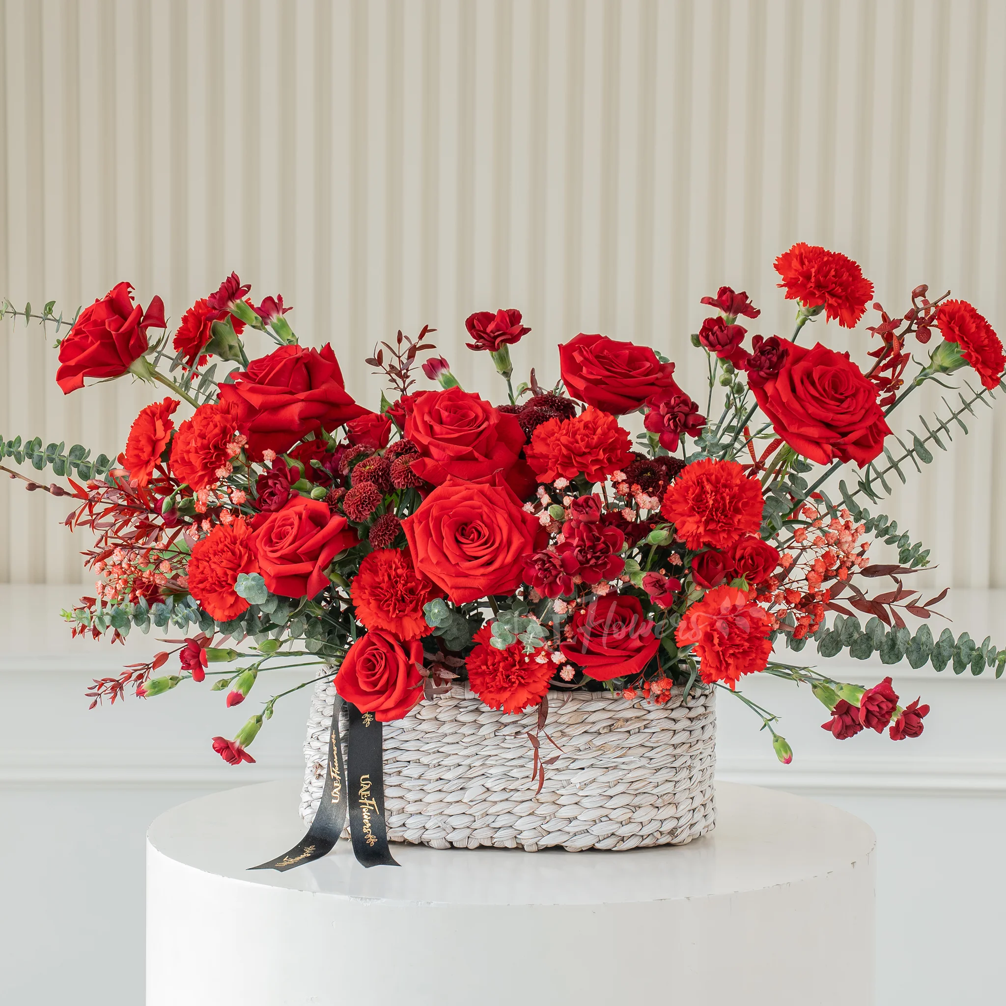 10 red roses, 12 red carnations and 6 red spray carnations with green fillers in a basket.
