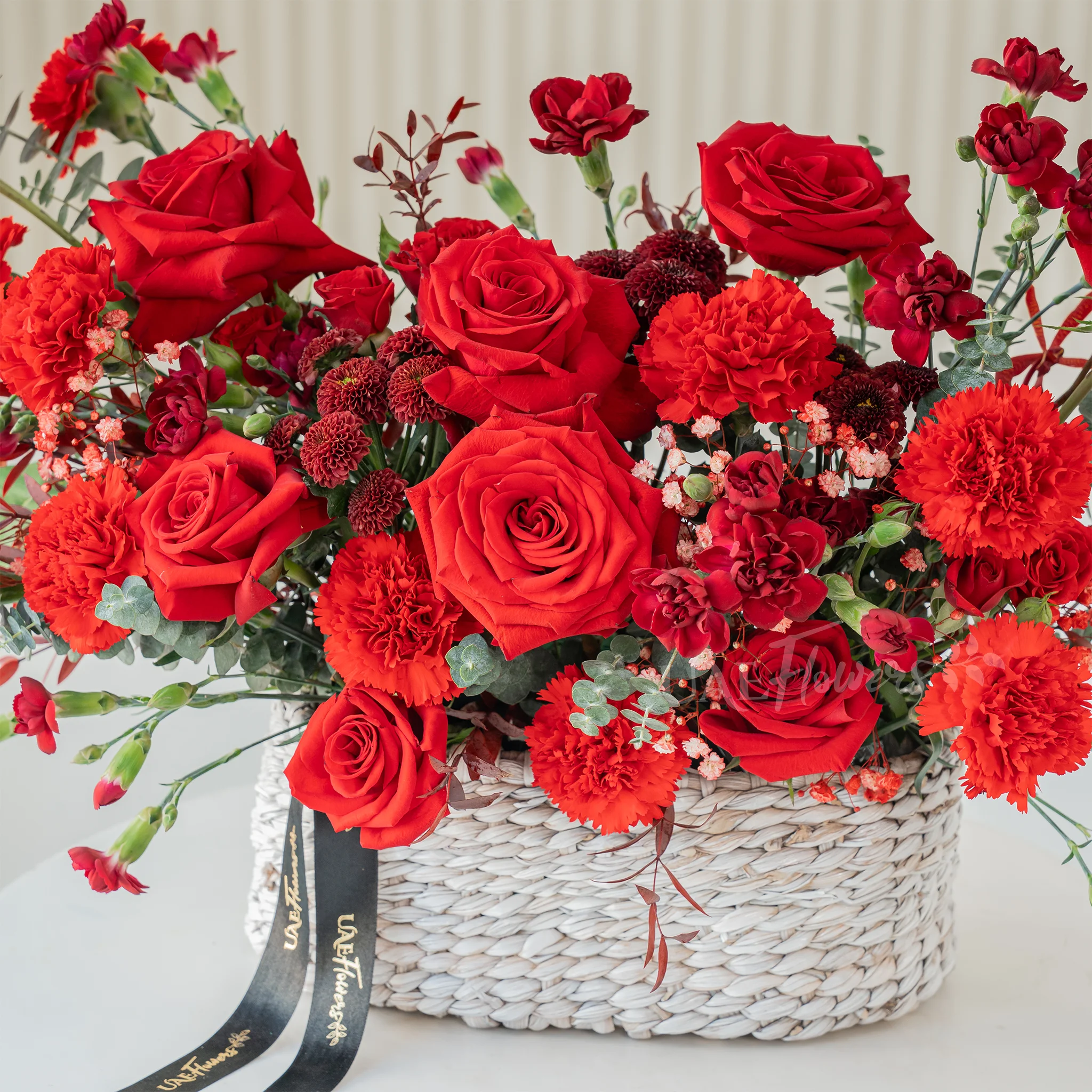 10 red roses, 12 red carnations and 6 red spray carnations with green fillers in a basket.