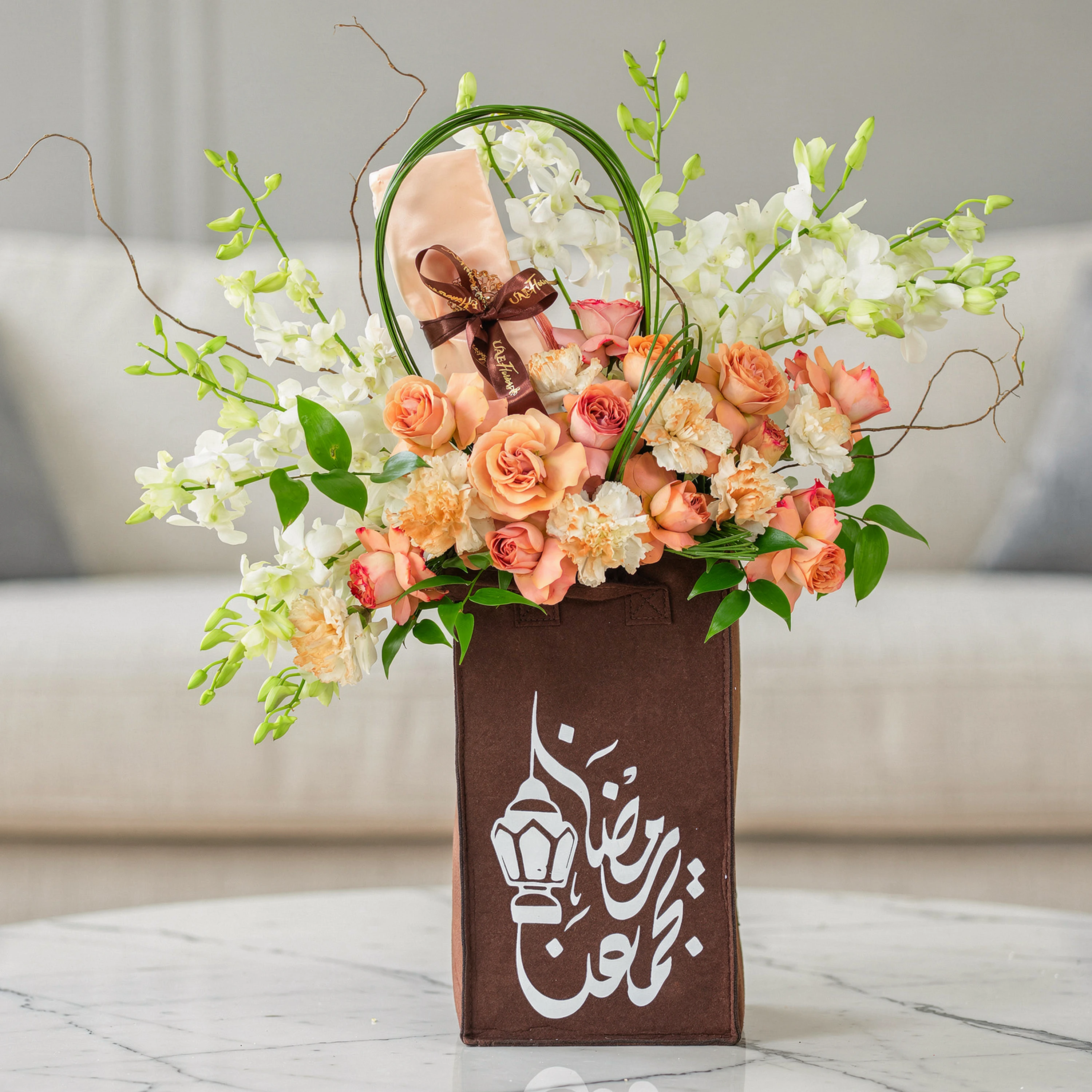 Arrangement of 7 peach carnations, 6 peach roses, spray peach roses and 10 white orchids with steel grass in a bag.