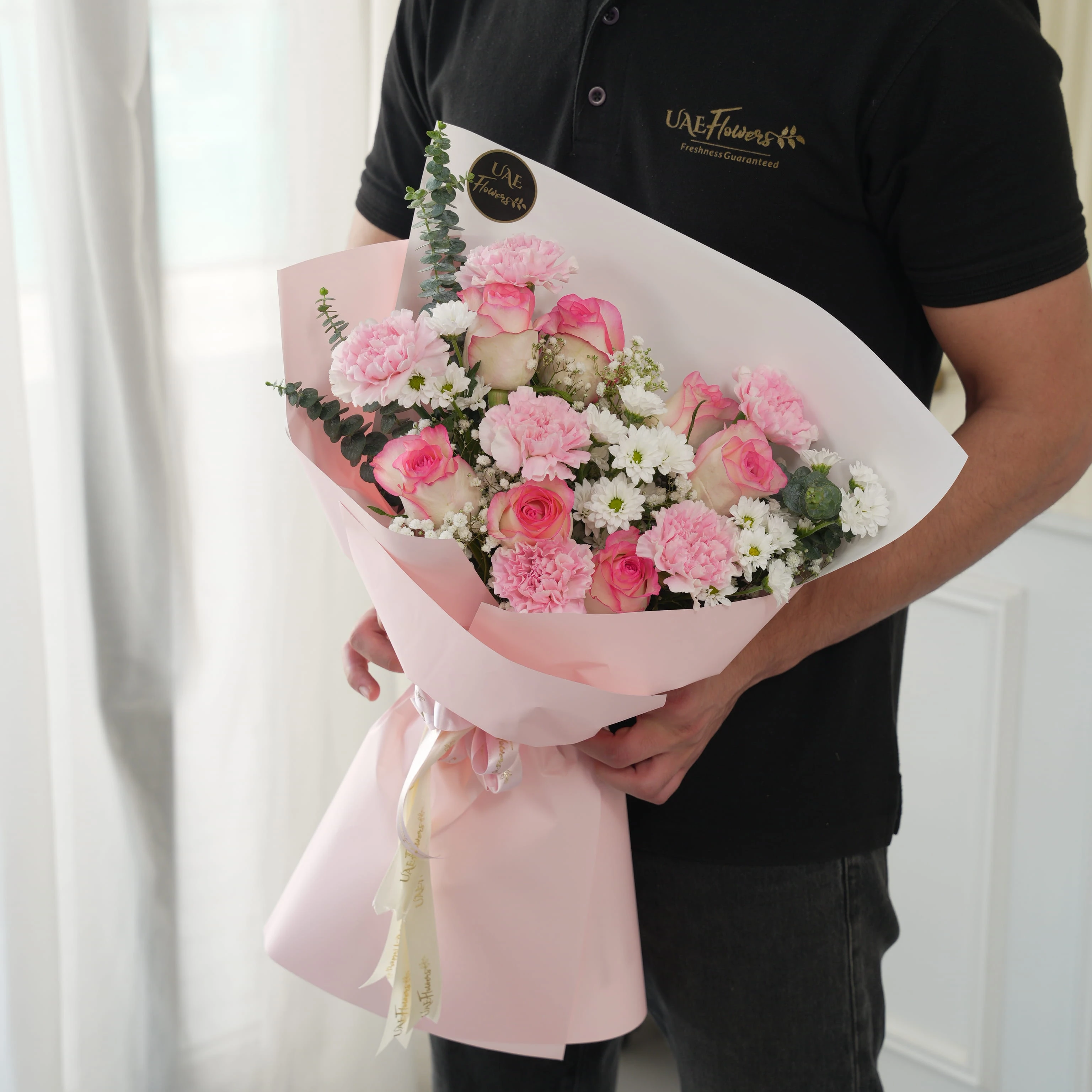 Bouquet of 7 pink roses, 6 pink carnations, 2 white chrysanthemums with green fillers in pink wrapping.