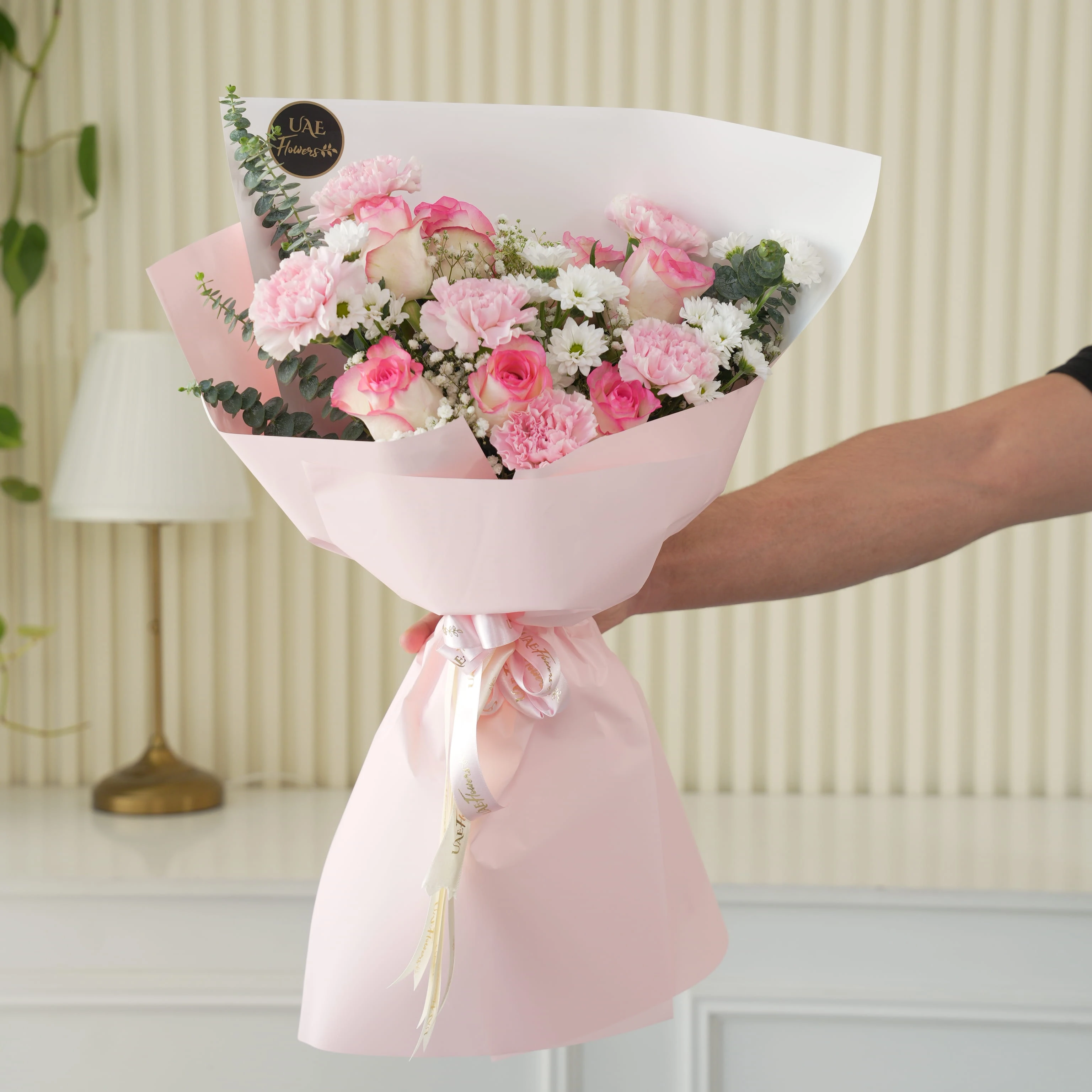 Bouquet of 7 pink roses, 6 pink carnations, 2 white chrysanthemums with green fillers in pink wrapping.