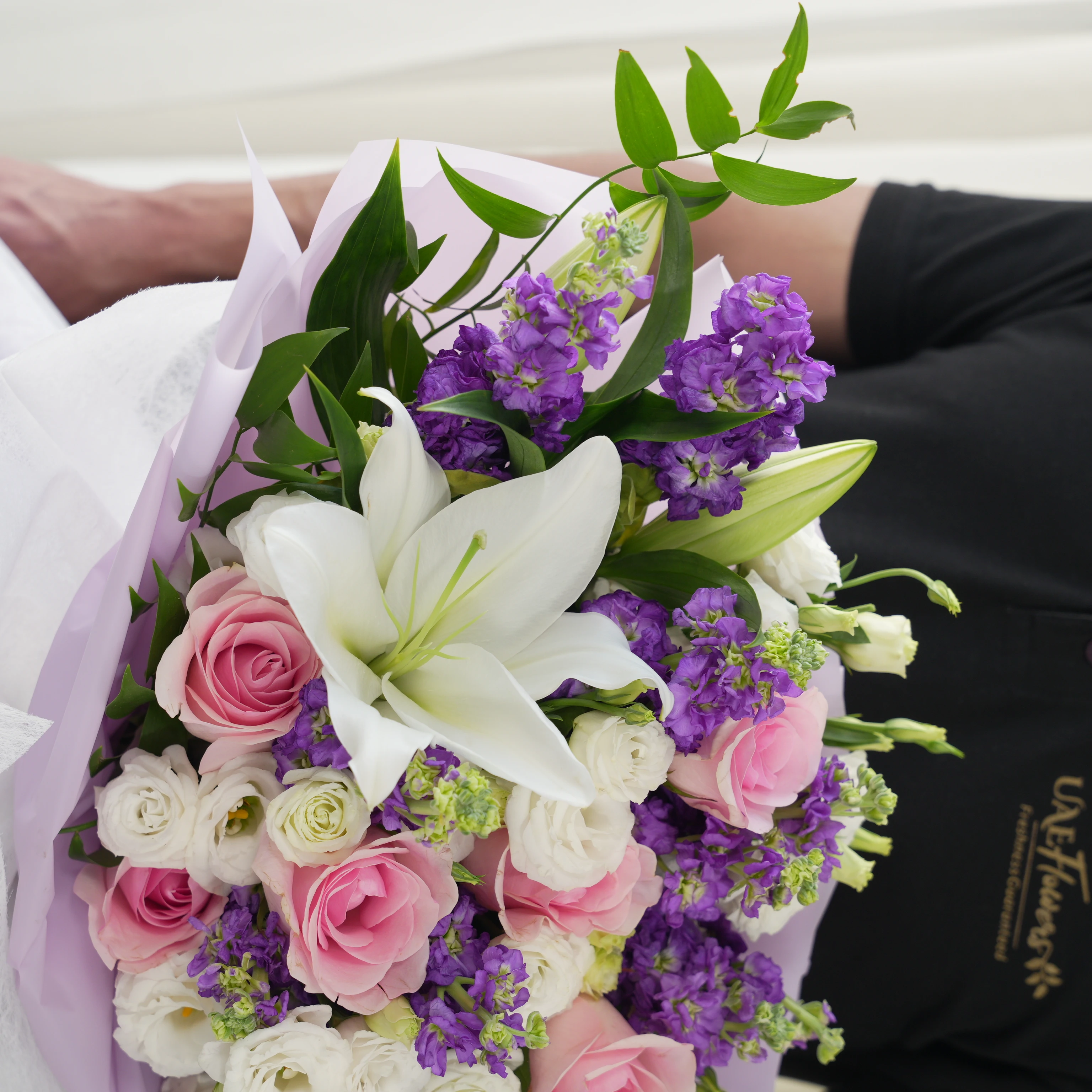 Bouquet of 2 white lilies, 10 purple matthiola, 5 white lisianthus and 8 pink roses with green fillers in nice wrapping.