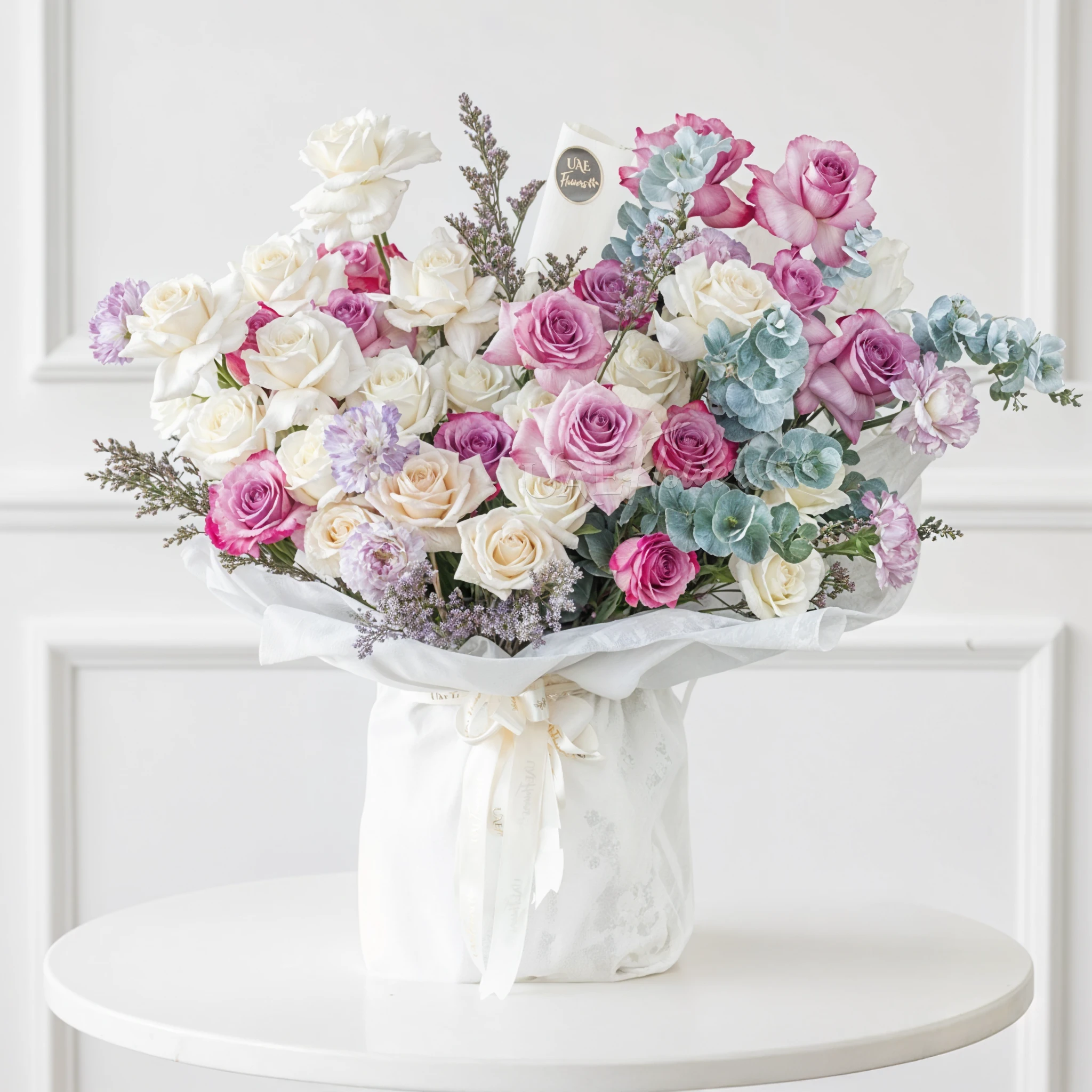 Bouquet of 20 white roses, 12 purple roses and 5 carnations with eucalyptus leaf and green fillers in white paper packing tied with white ribbon.
