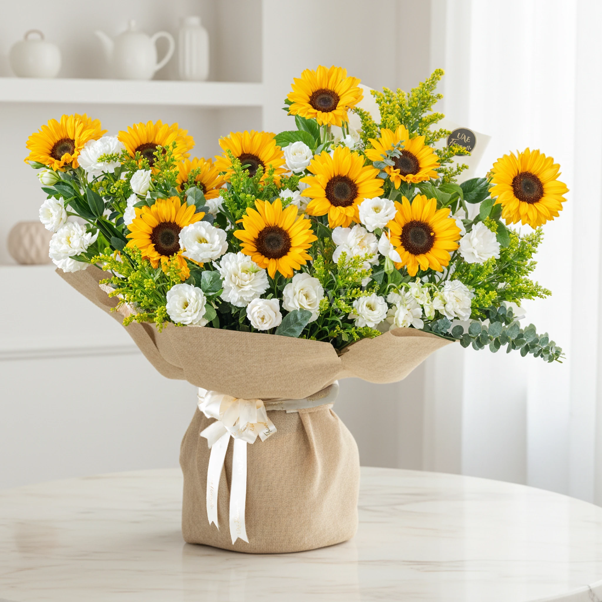 Bouquet of 11 sunflowers and 10 white lisianthus with green fillers and yellow statis in brown paper packing tied with white ribbon.