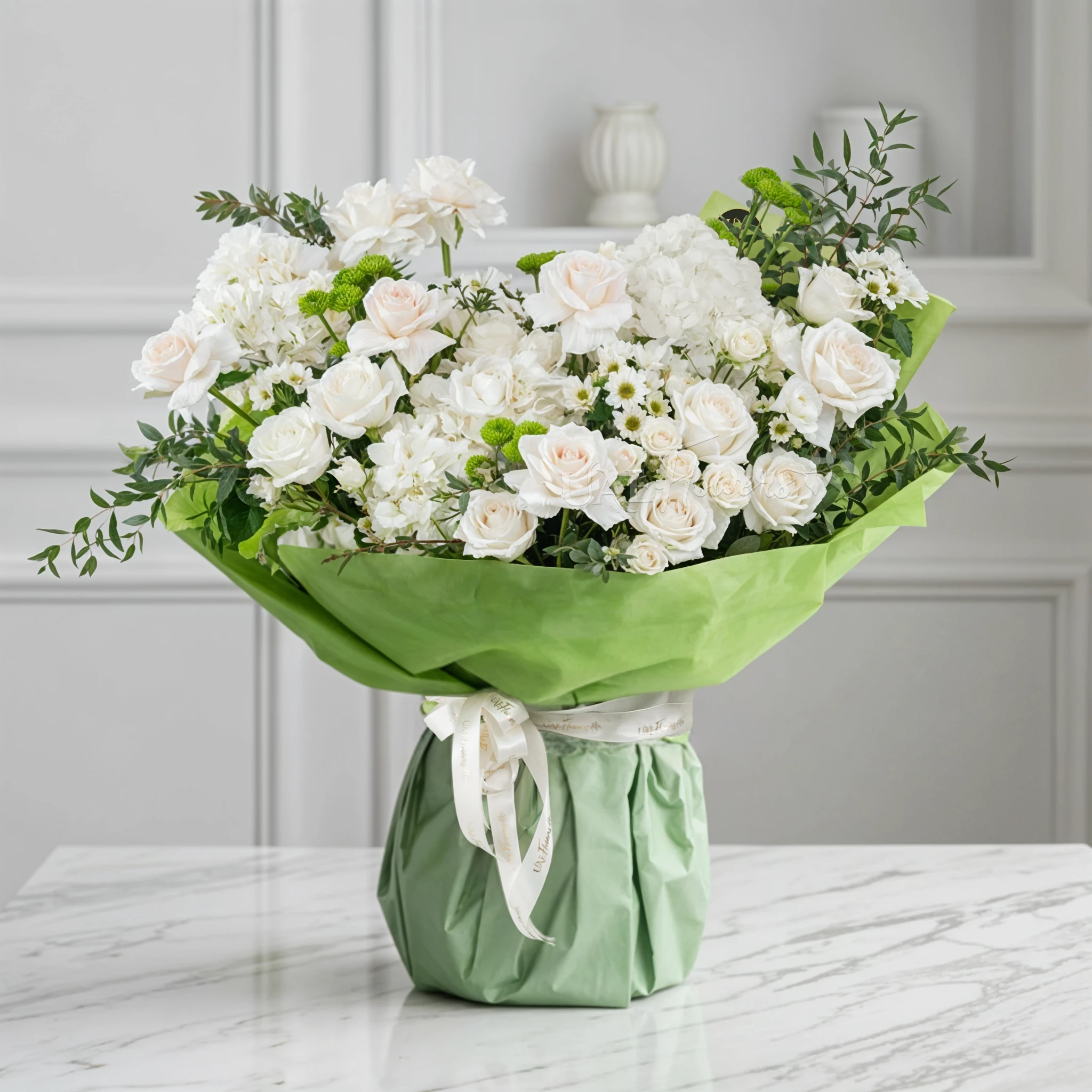 Bouquet of 16 white roses, 4 green button chrysanthemums, 3 white hydrangeas, 3 white spray roses and 4 white chrysanthemums with green fillers in green paper packing tied with white ribbon.