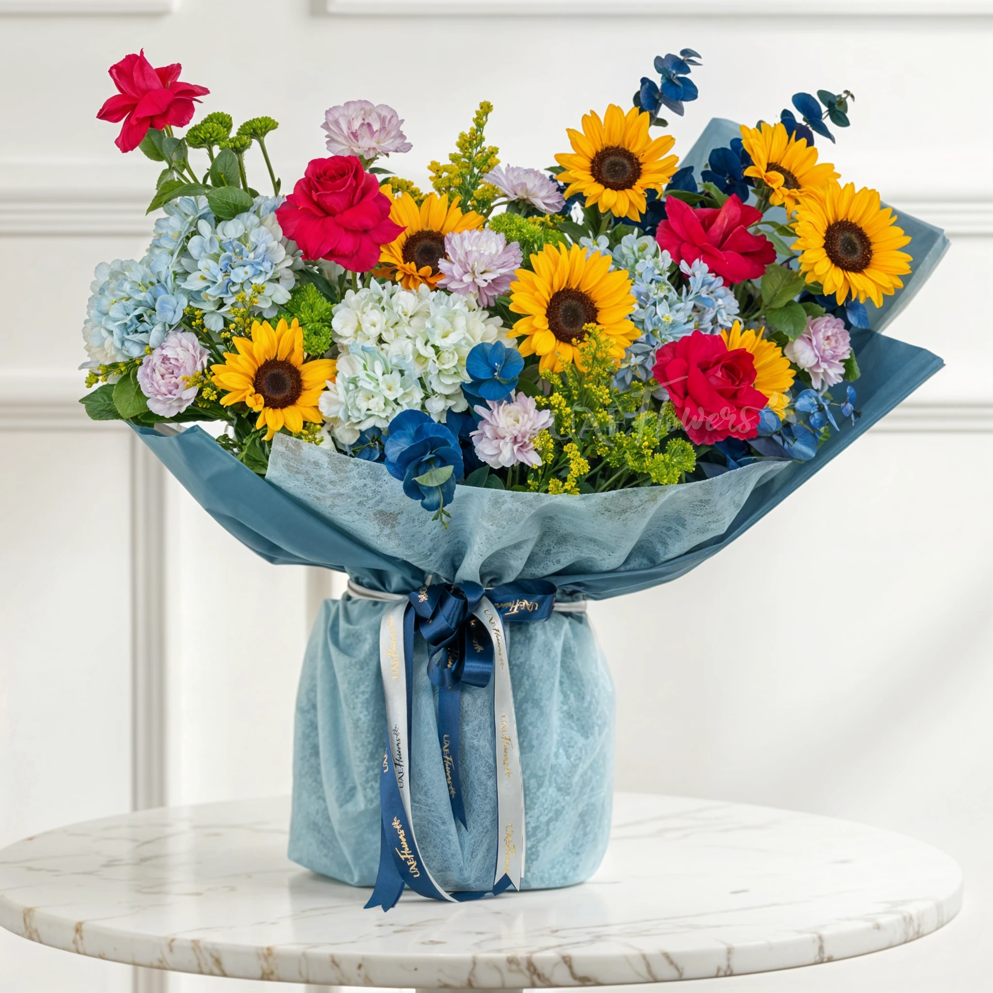 Bouquet of 8 sunflowers, 4 red roses, 5 blue hydrangeas, 6 carnations, green button chrysanthemums, blue sprayed eucalyptus leaf with green fillers in blue paper packing tied with blue ribbons.