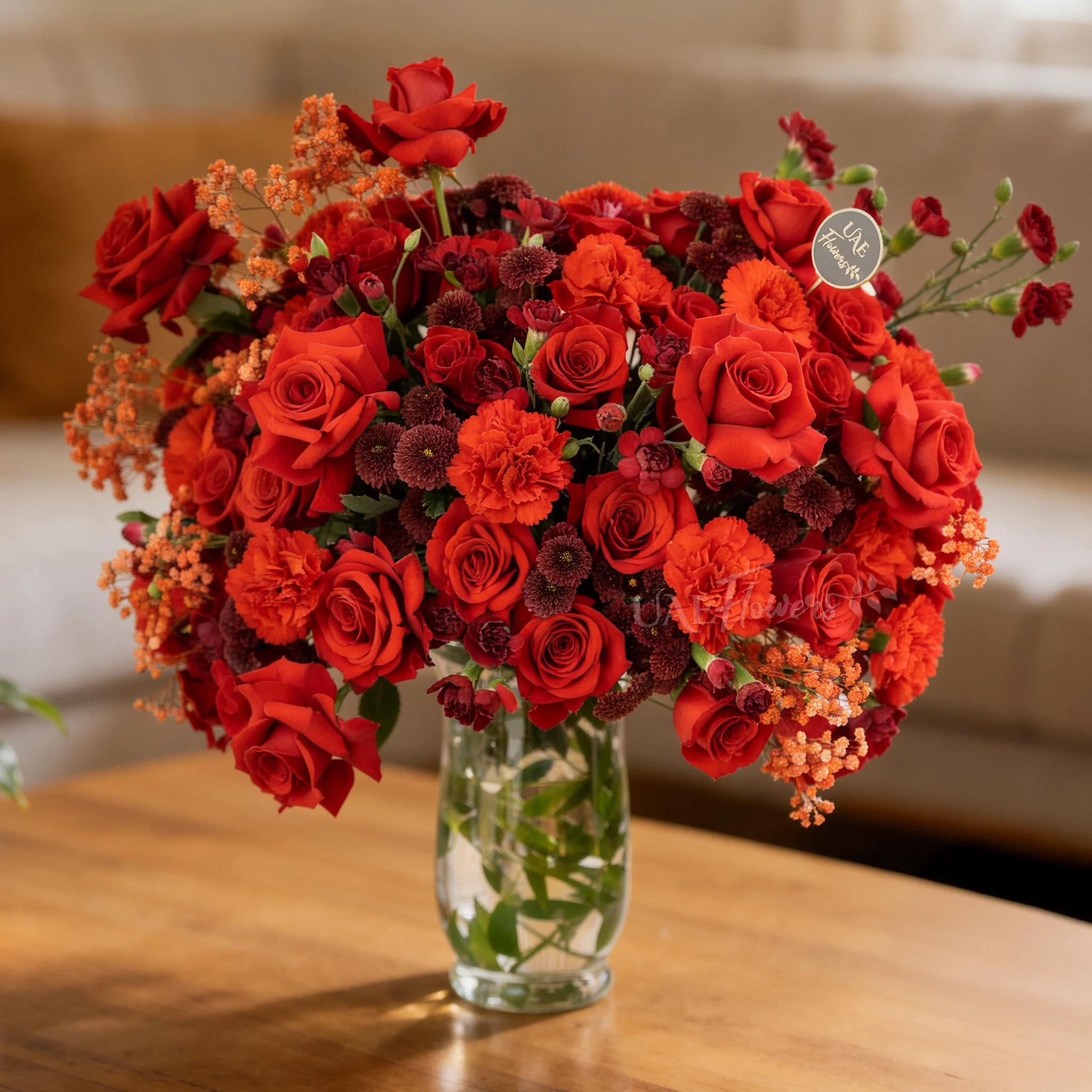 One-side arrangement of 20 red roses, 7 red chrysanthemums, 8 red carnations and 4 red spray carnations with green fillers in a glass vase.