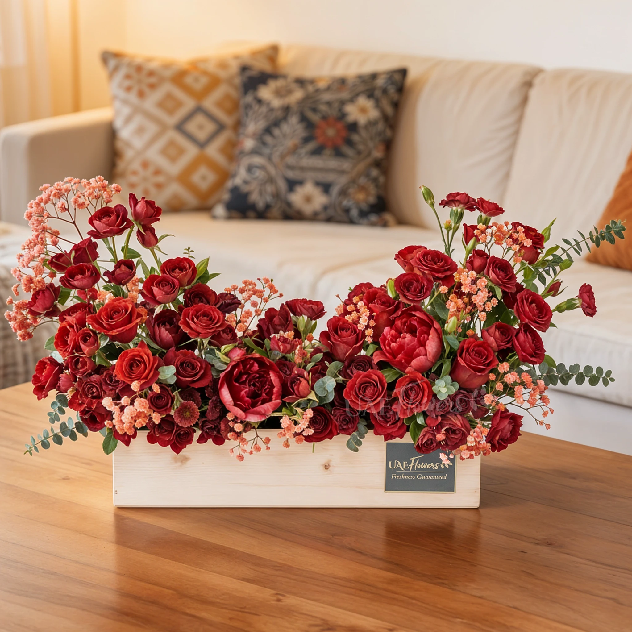 An arrangement of 10 red roses, 10 red spray roses and 3 red peonies with green fillers in a wooden tray.