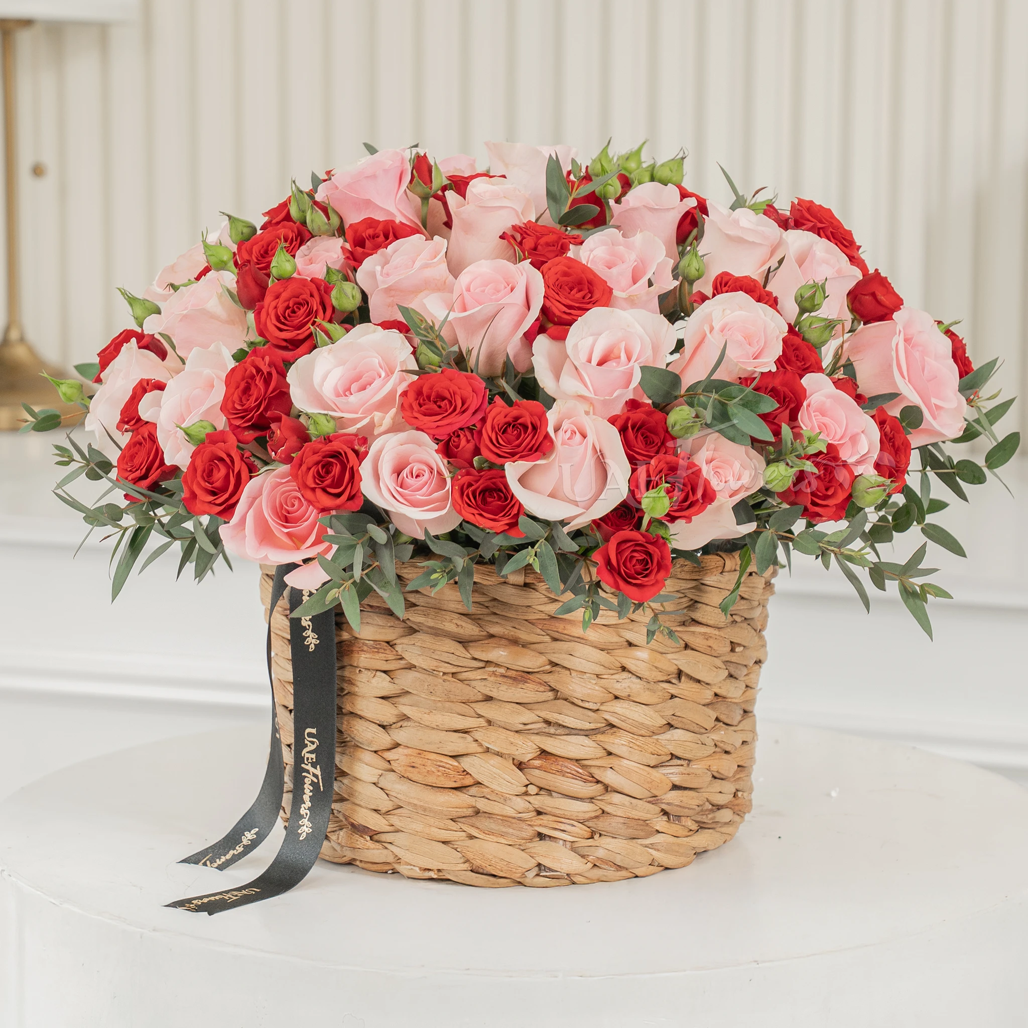 25 pink roses and 12 red spray roses with green fillers in a round basket.