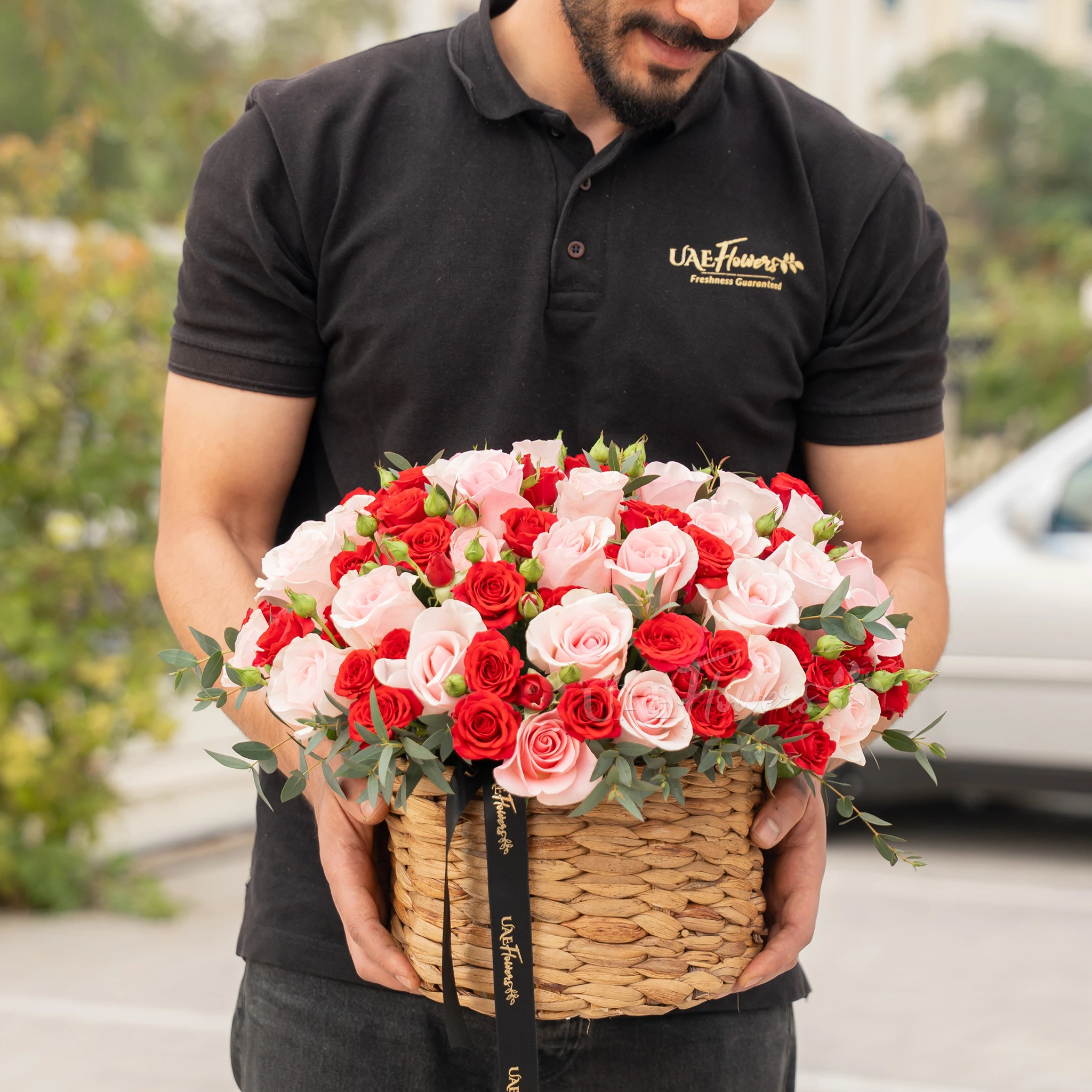 25 pink roses and 12 red spray roses with green fillers in a round basket.