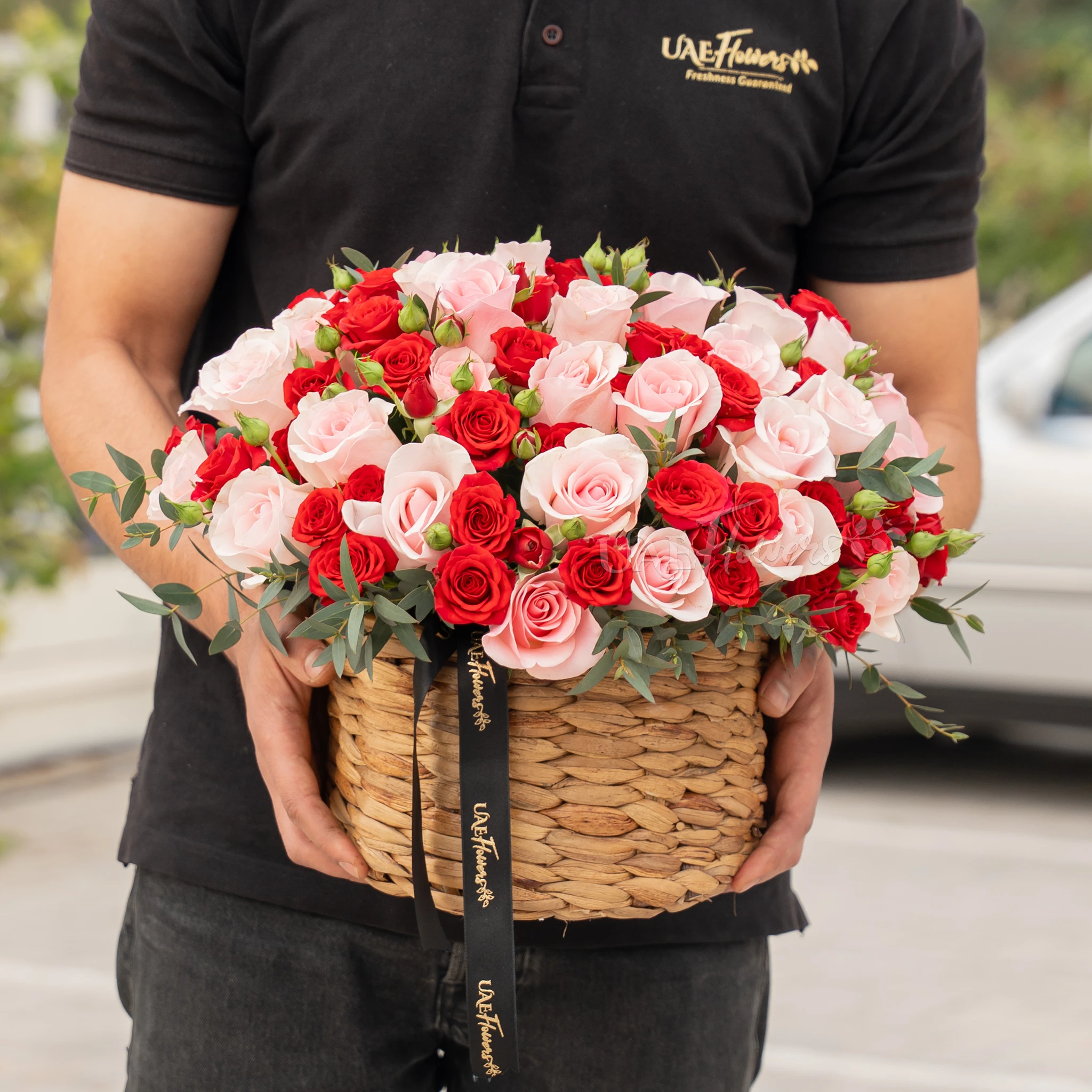 25 pink roses and 12 red spray roses with green fillers in a round basket.