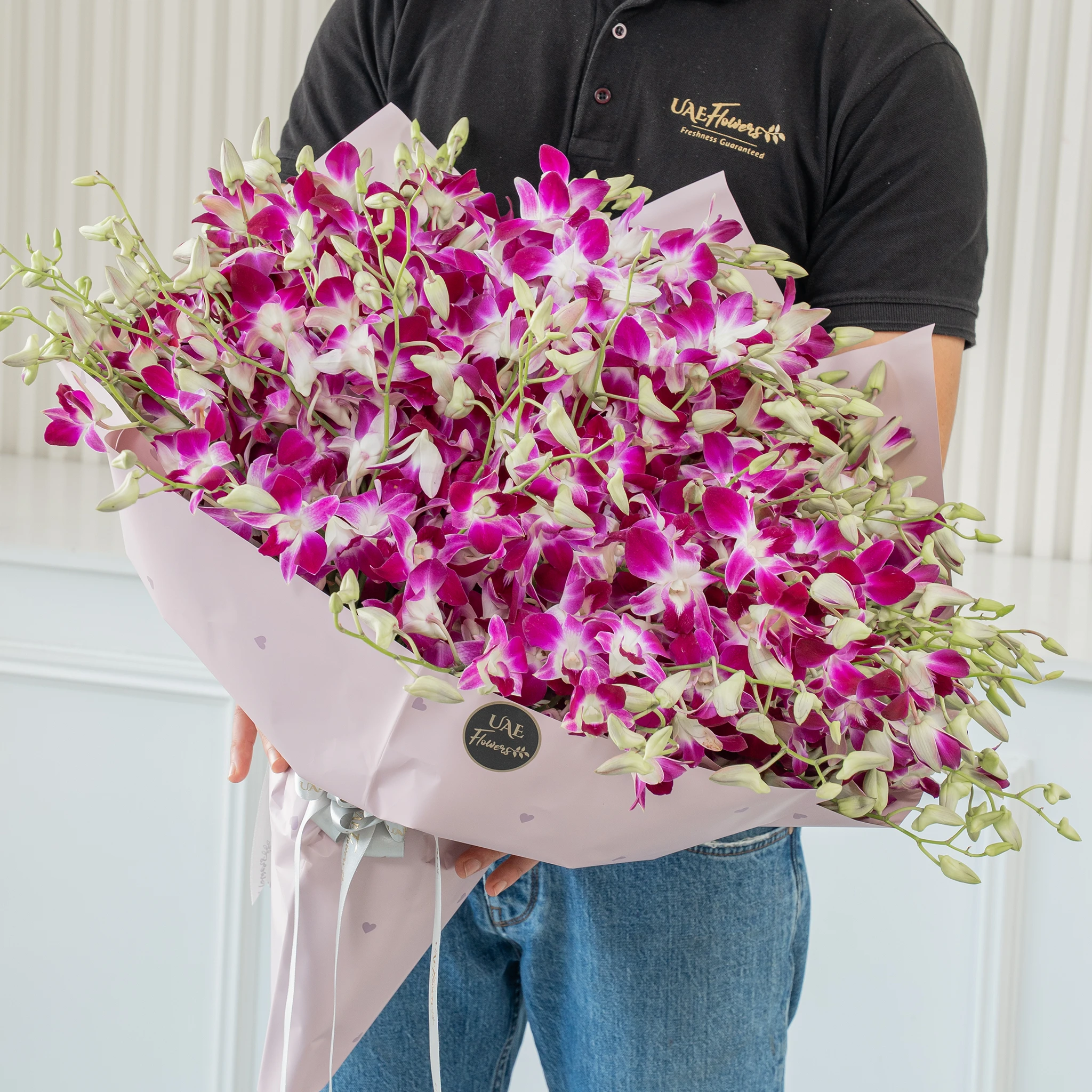 Bouquet of 100 purple orchids with fillers in a pink wrapping paper.