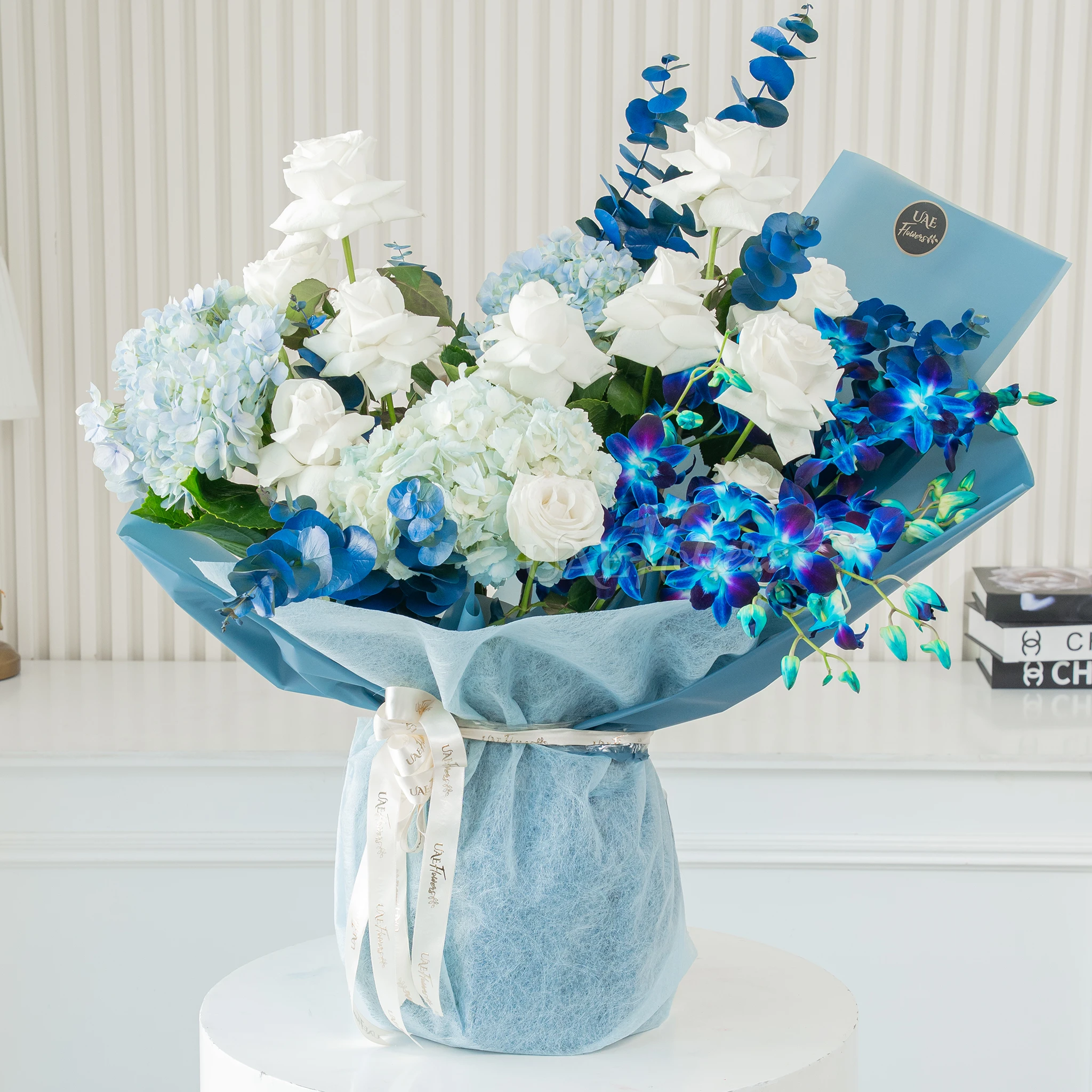 Bouquet of blue hydrangeas, white roses, and blue orchids wrapped in blue paper, a serene floral arrangement for special celebrations.