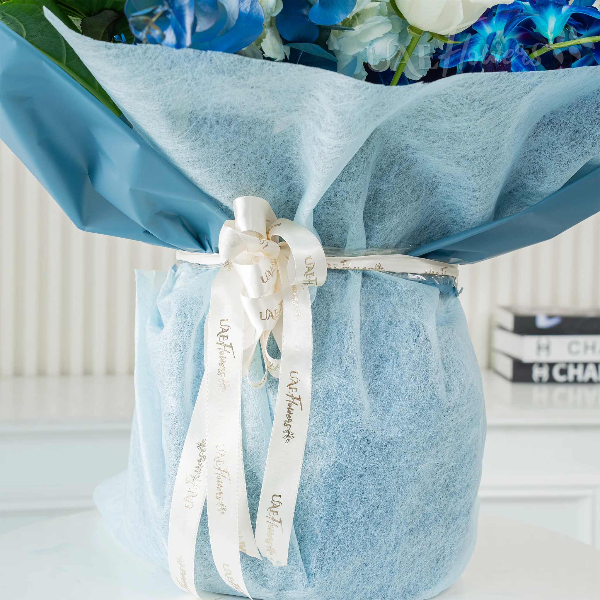 Bouquet of blue hydrangeas, white roses, and blue orchids wrapped in blue paper, a serene floral arrangement for special celebrations.