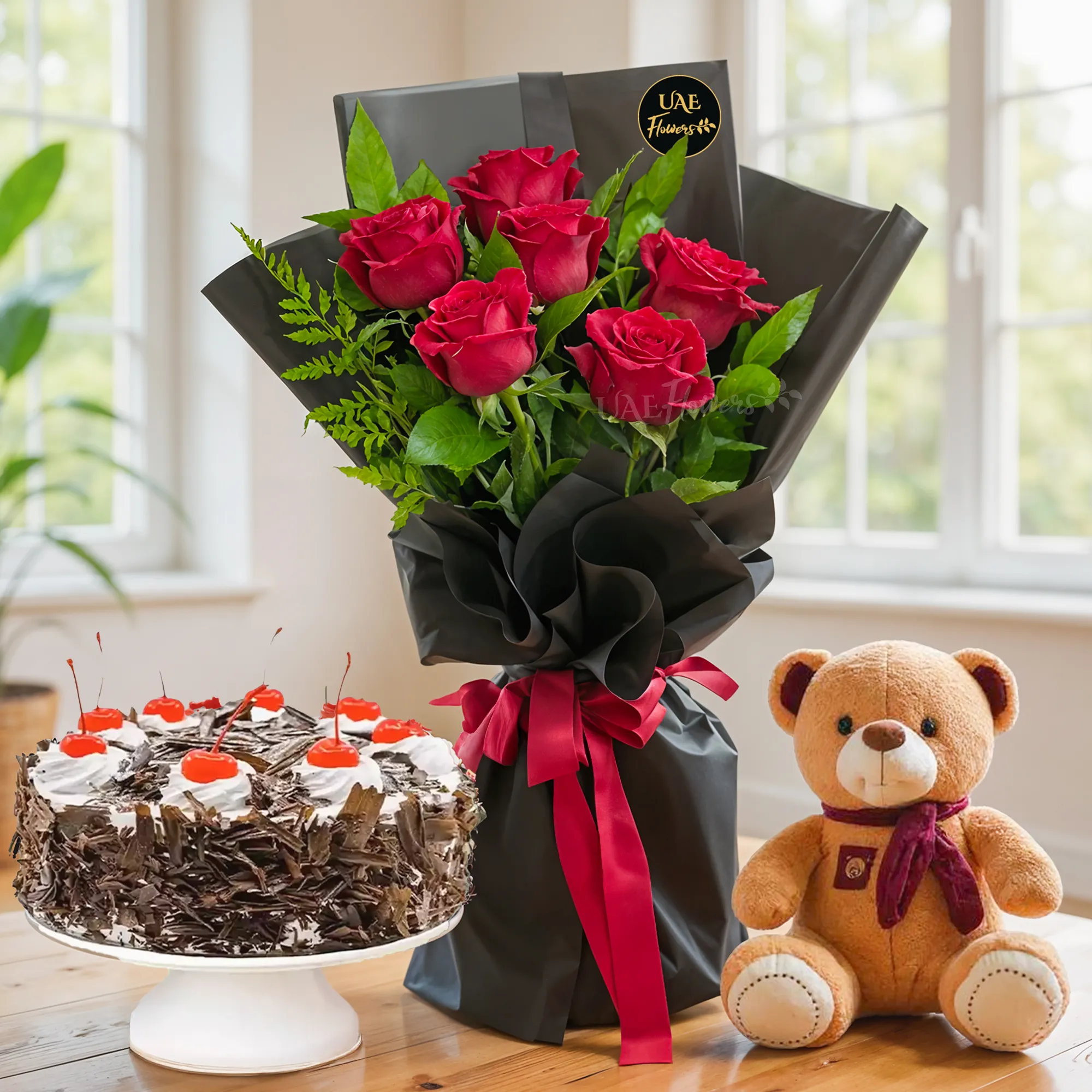Bouquet of 6 red roses with green fillers in black wrapping, 1 kg black forest cake and a small brown teddy bear.