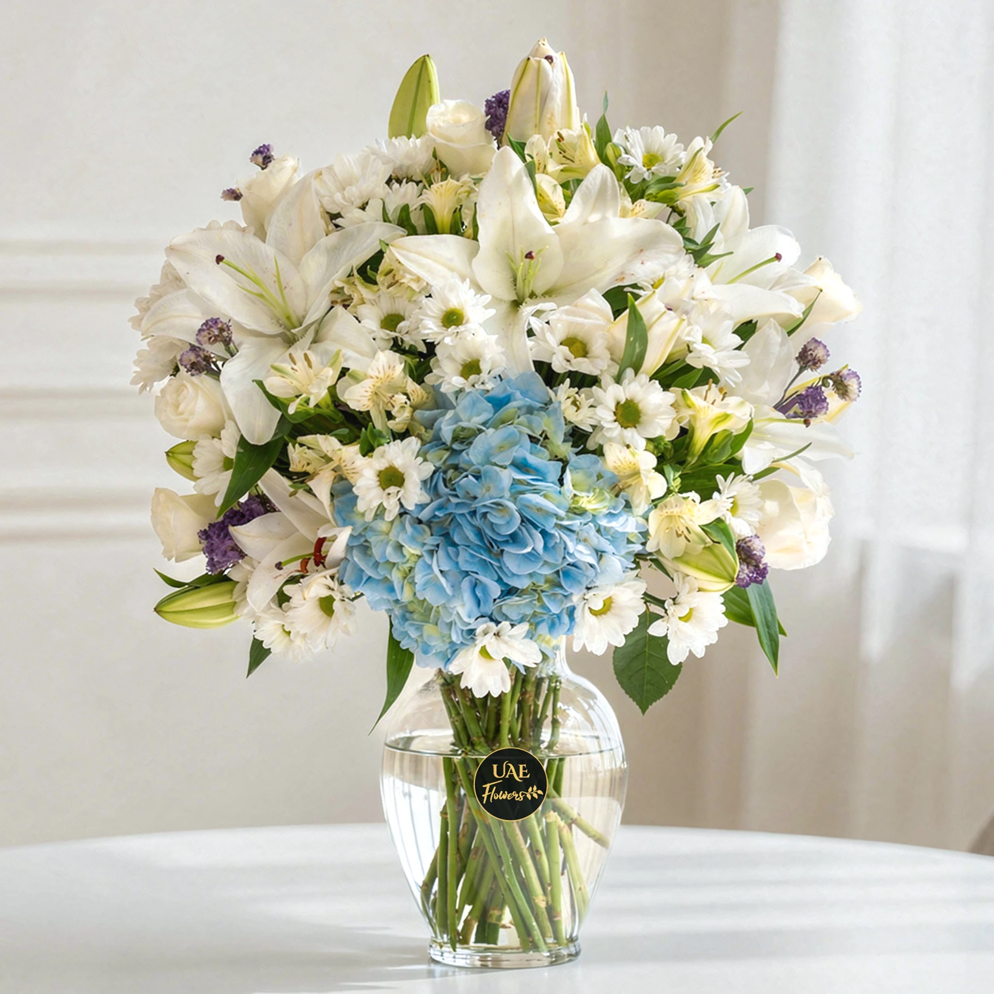 3 alstroemeria, 4 white chrysanthemums, 3 white roses, 2 white Lilies, 3 purple statice, and blue hydrangea in a clear glass vase