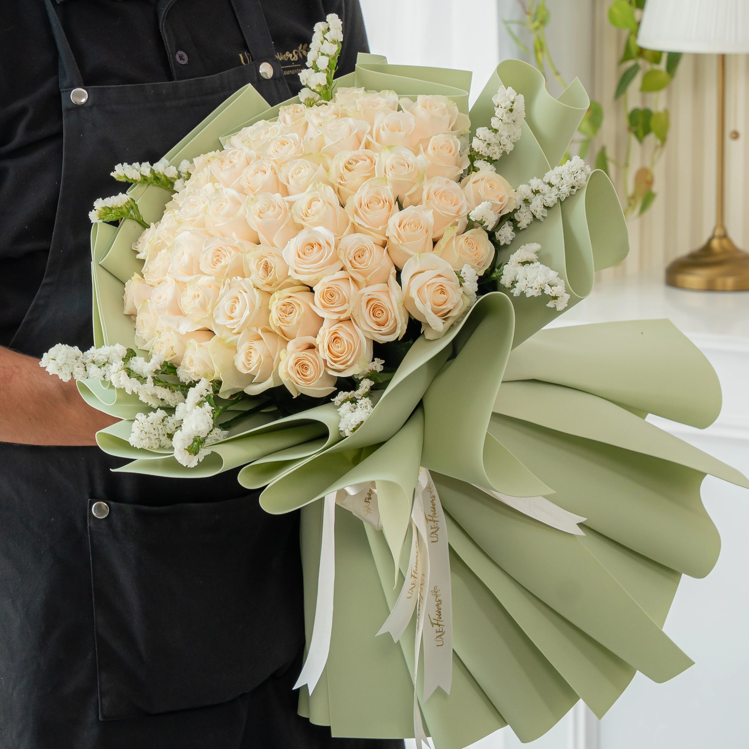 Bouquet of 40 white roses with white statice fillers in green foam paper tied with ribbons.
