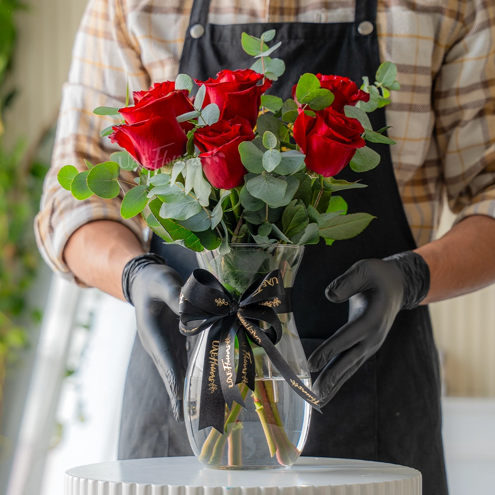 6 red roses arranged in a glass vase with eucalyptus