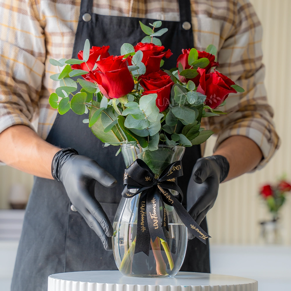 6 red roses arranged in a glass vase with eucalyptus
