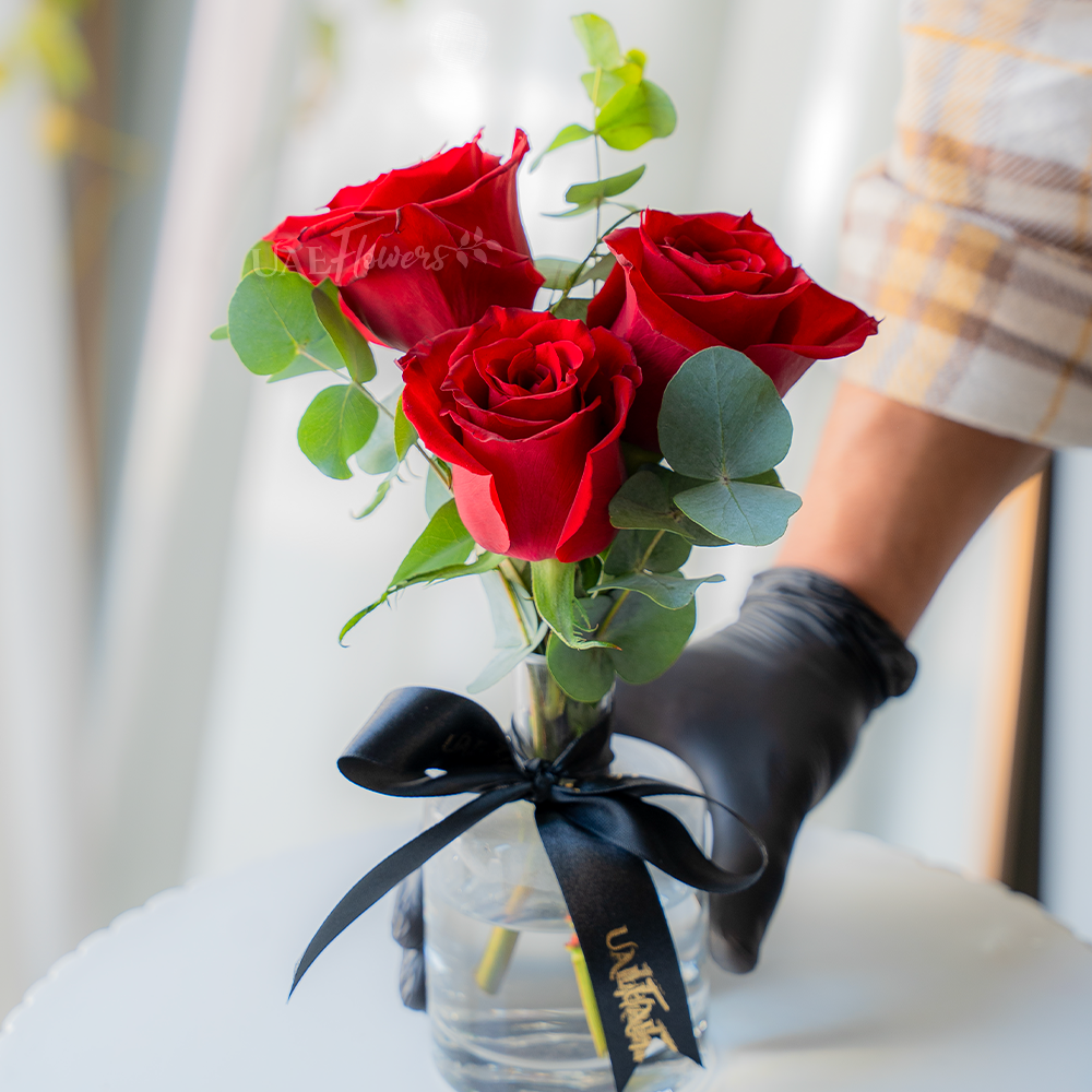 3 red roses with green fillers in a glass vase.