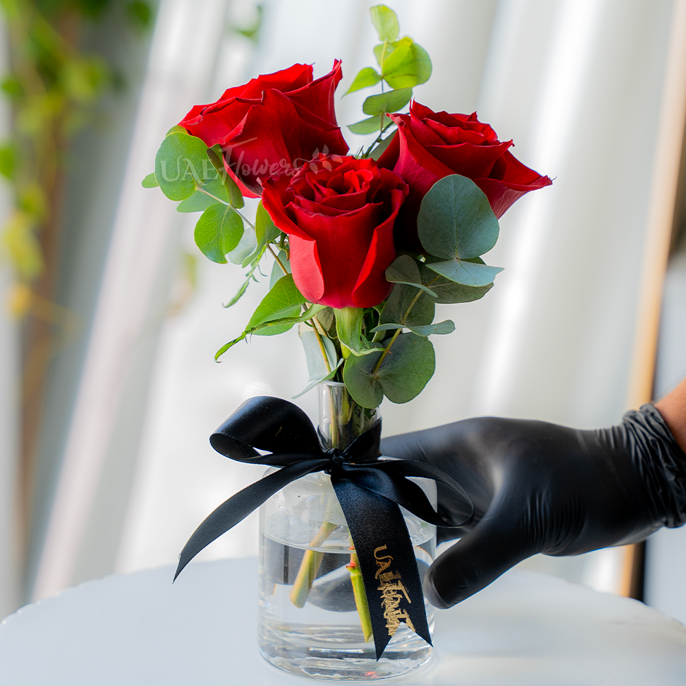 3 red roses with green fillers in a glass vase.