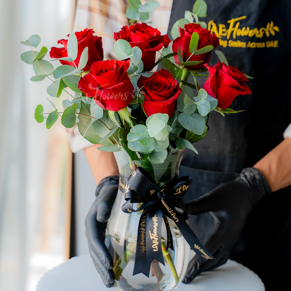 6 red roses arranged in a glass vase with eucalyptus