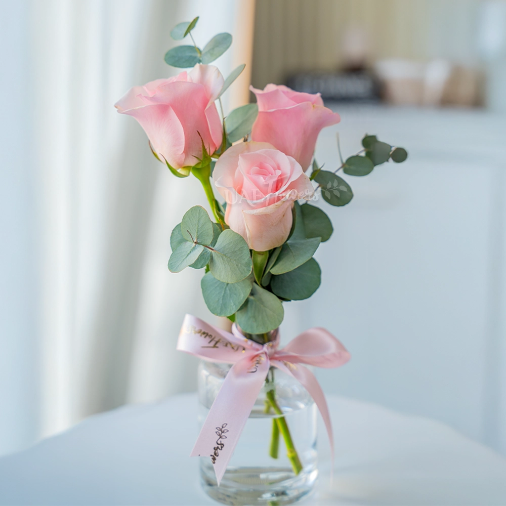 3 pink roses in a clear vase with eucalyptus