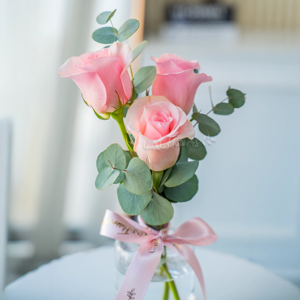 3 pink roses in a clear vase with eucalyptus