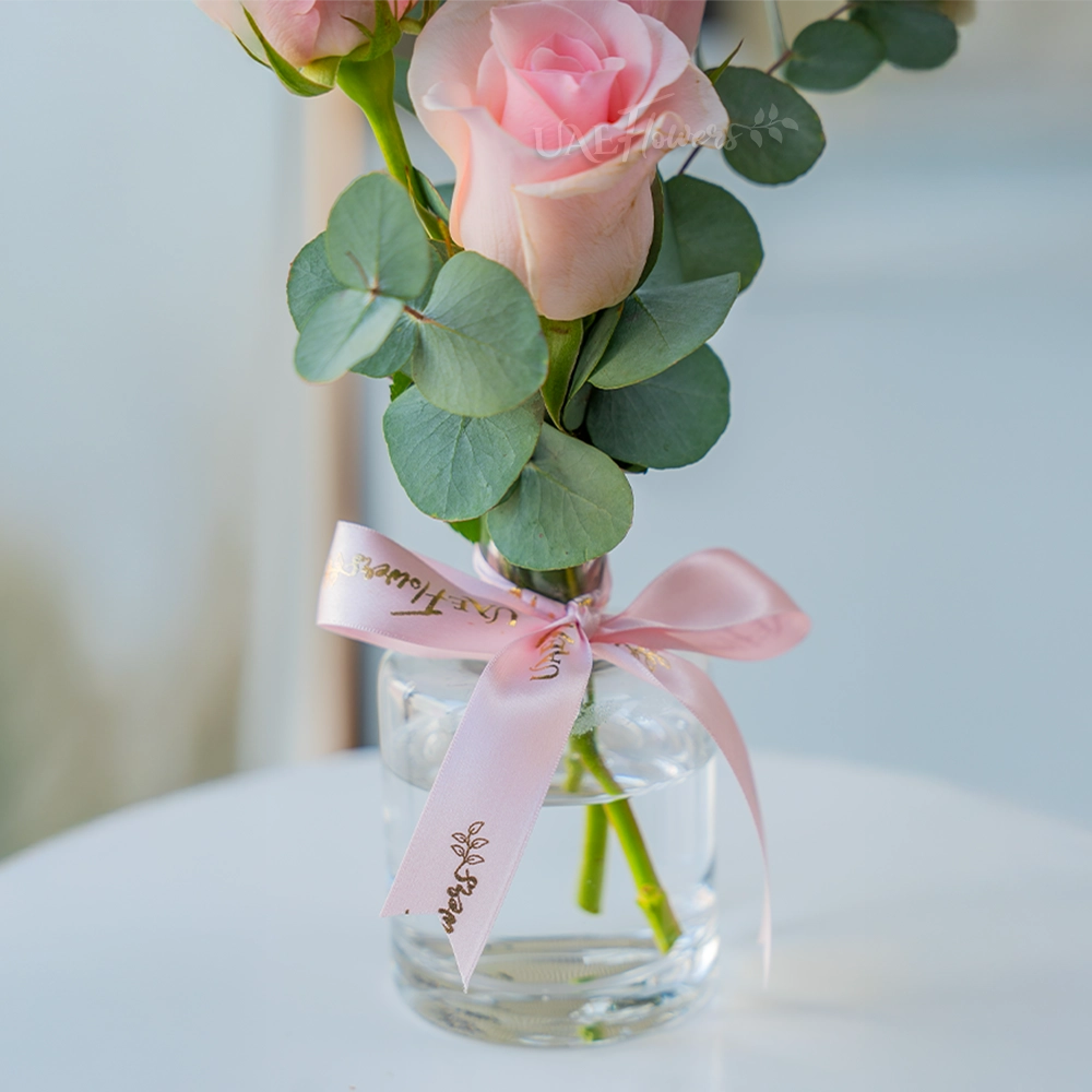 3 pink roses in a clear vase with eucalyptus