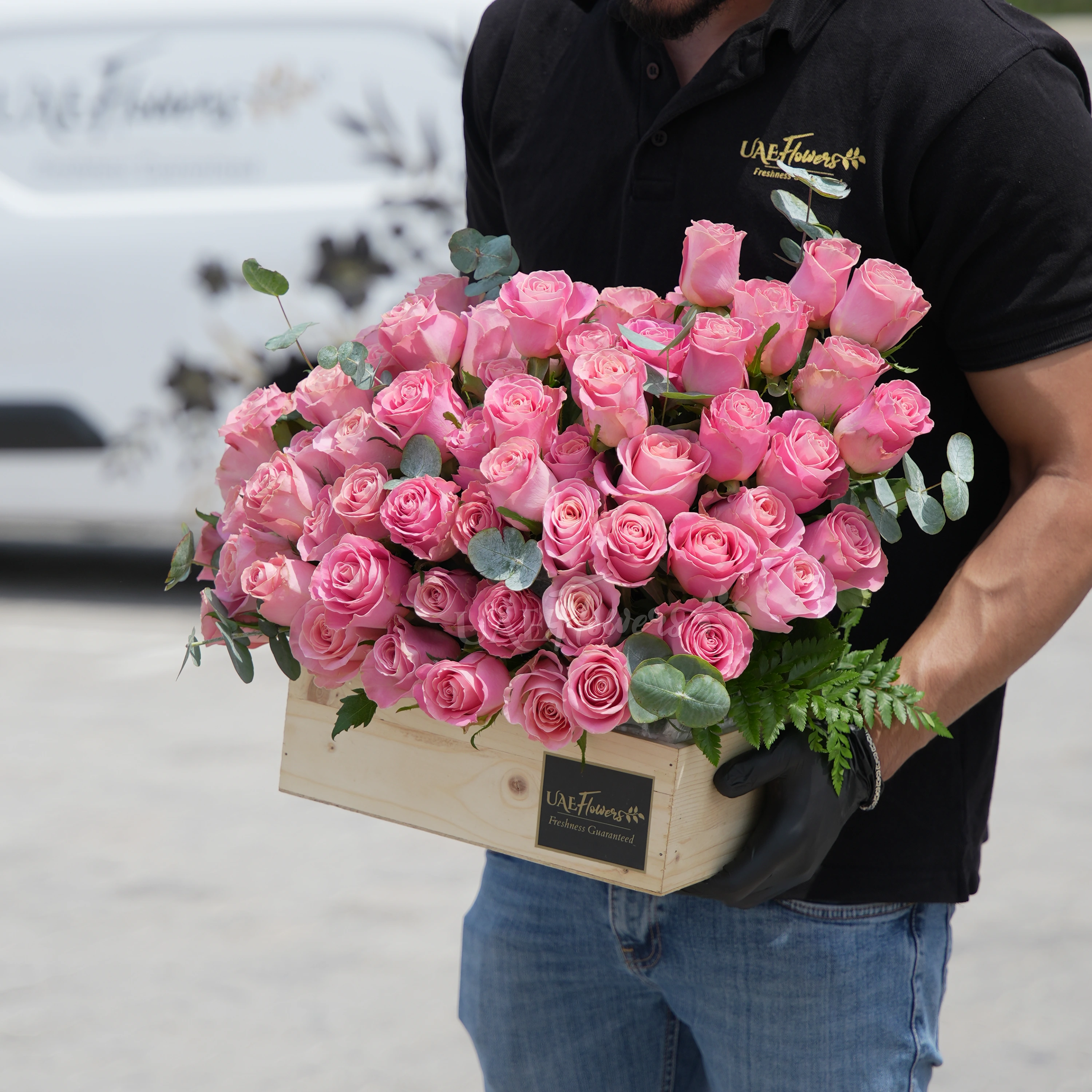 50 Hermosa pink roses in a wooden tray with eucalyptus leaves.