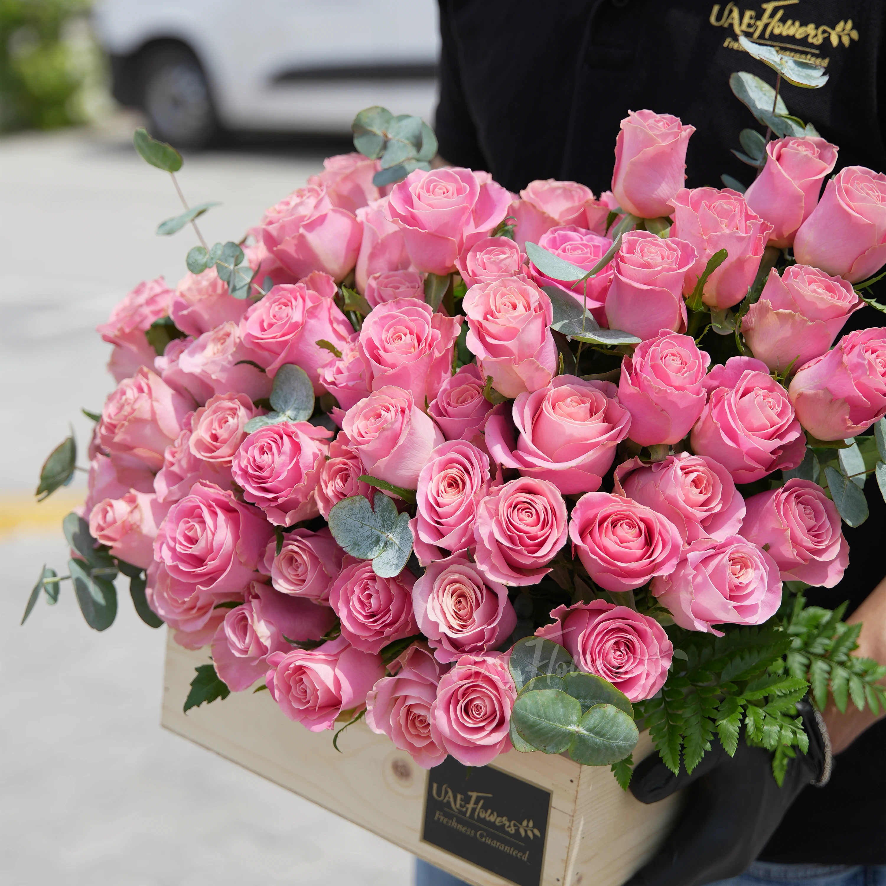50 Hermosa pink roses in a wooden tray with eucalyptus leaves.
