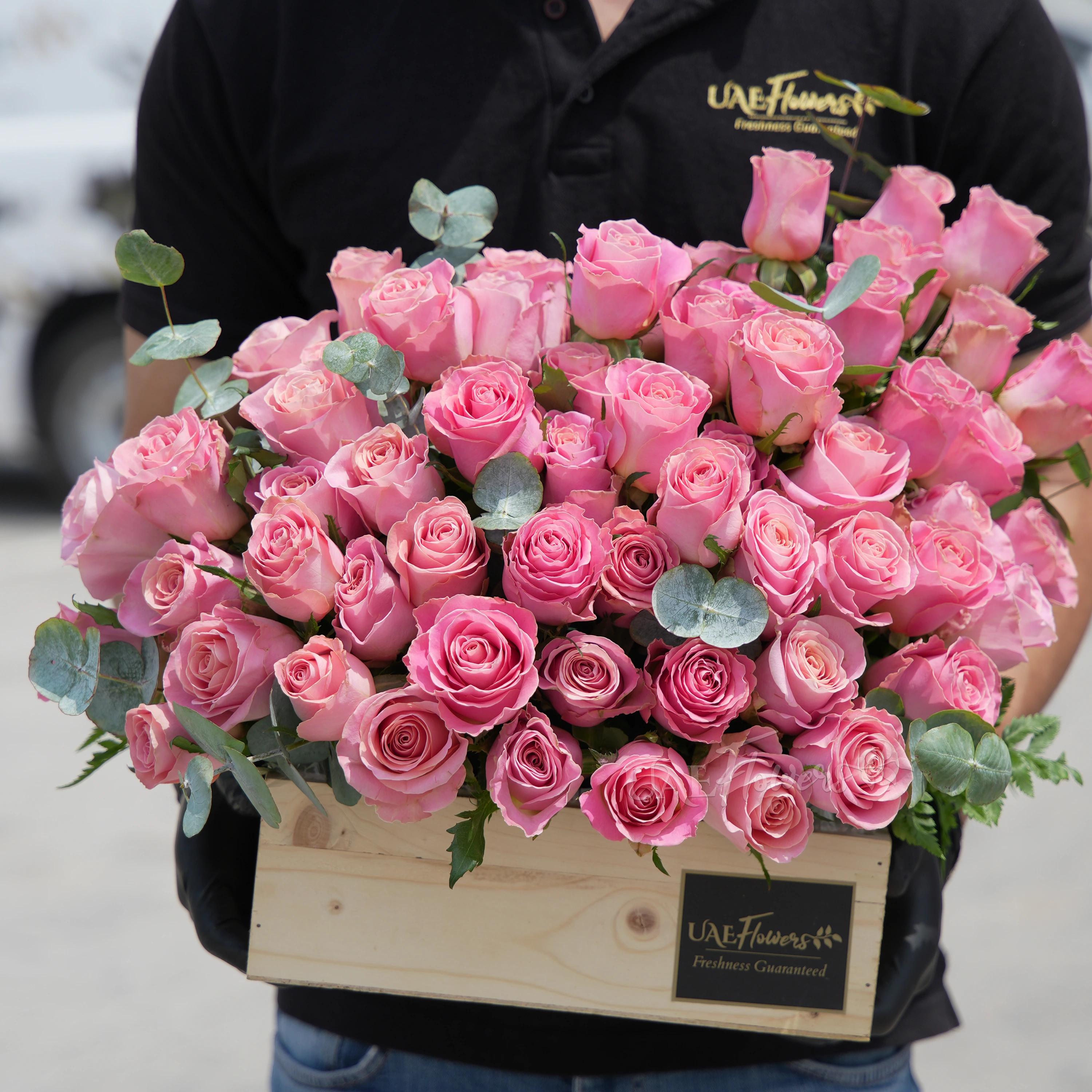 50 Hermosa pink roses in a wooden tray with eucalyptus leaves.