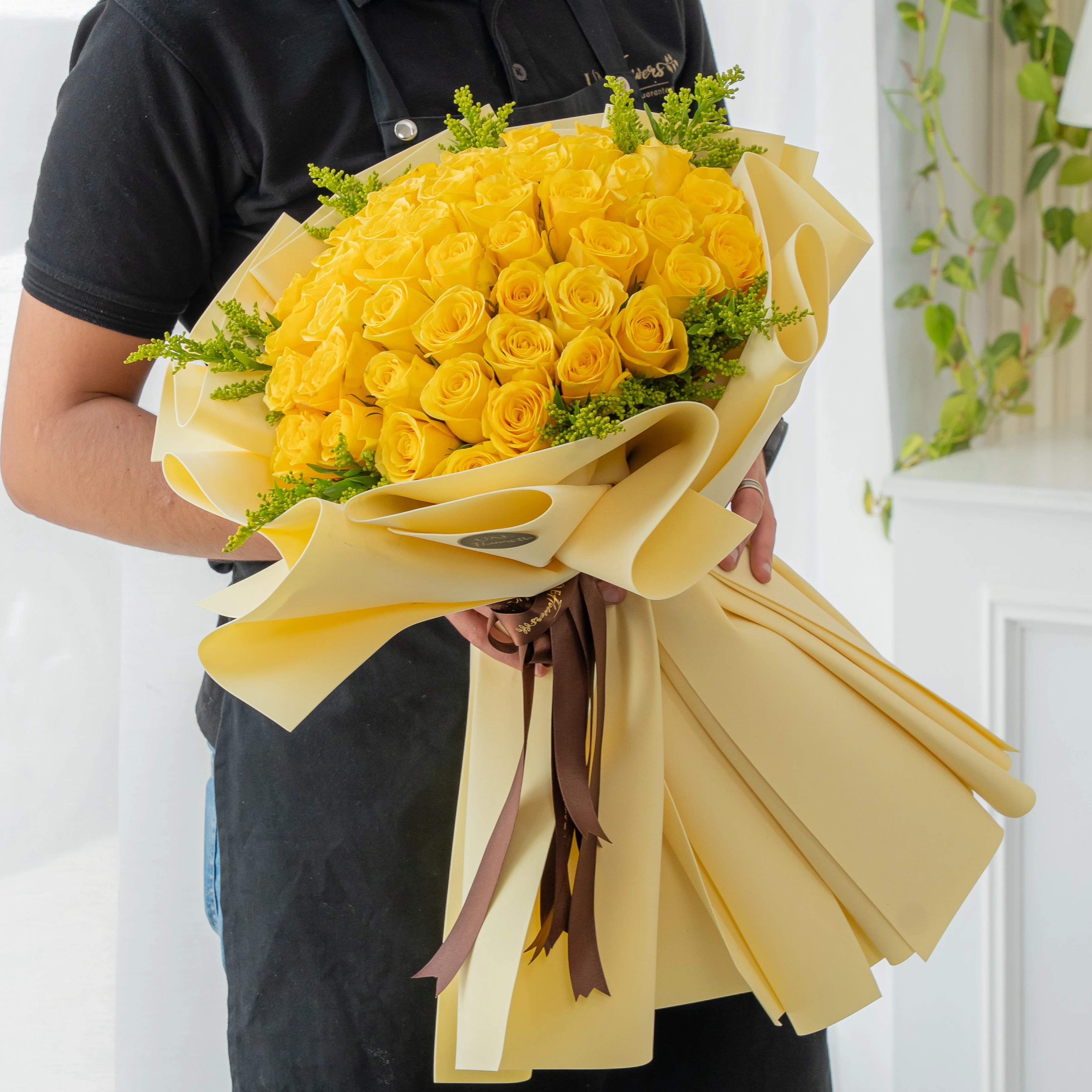 Bouquet of 40 white roses with solidago fillers in yellow foam paper tied with ribbons.