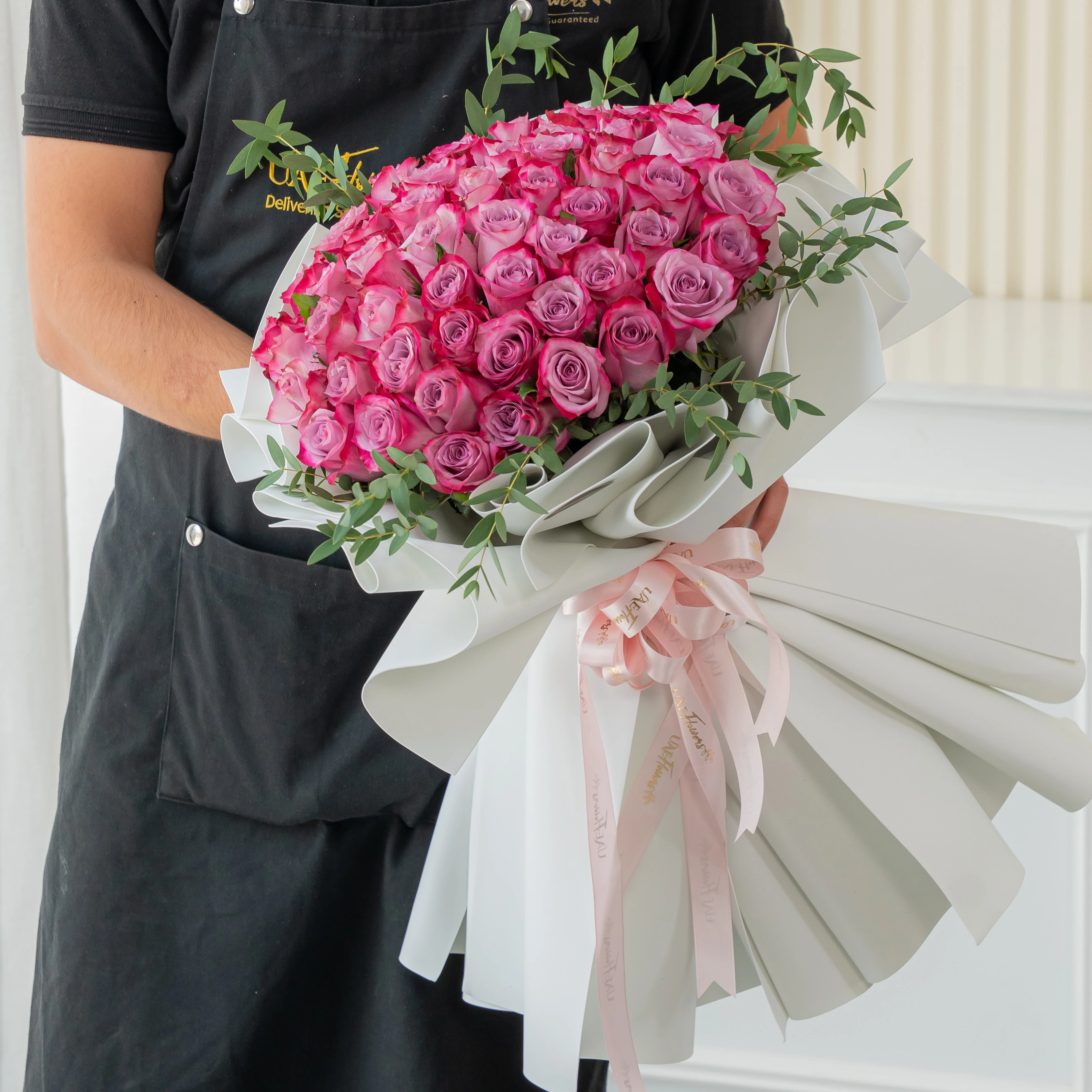 Bouquet of 40 purple roses with eucalyptus leaves in white foam paper tied with ribbons.