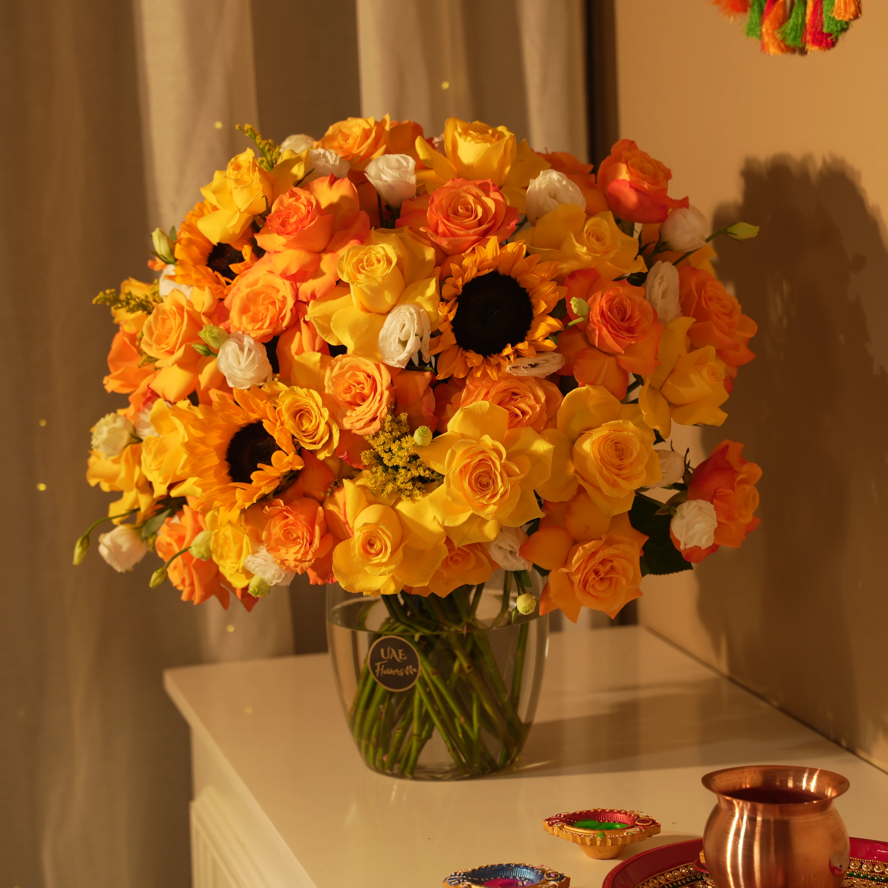 Yellow, orange, and white roses with sunflowers in glass vase for Diwali by UAE Flowers Dubai