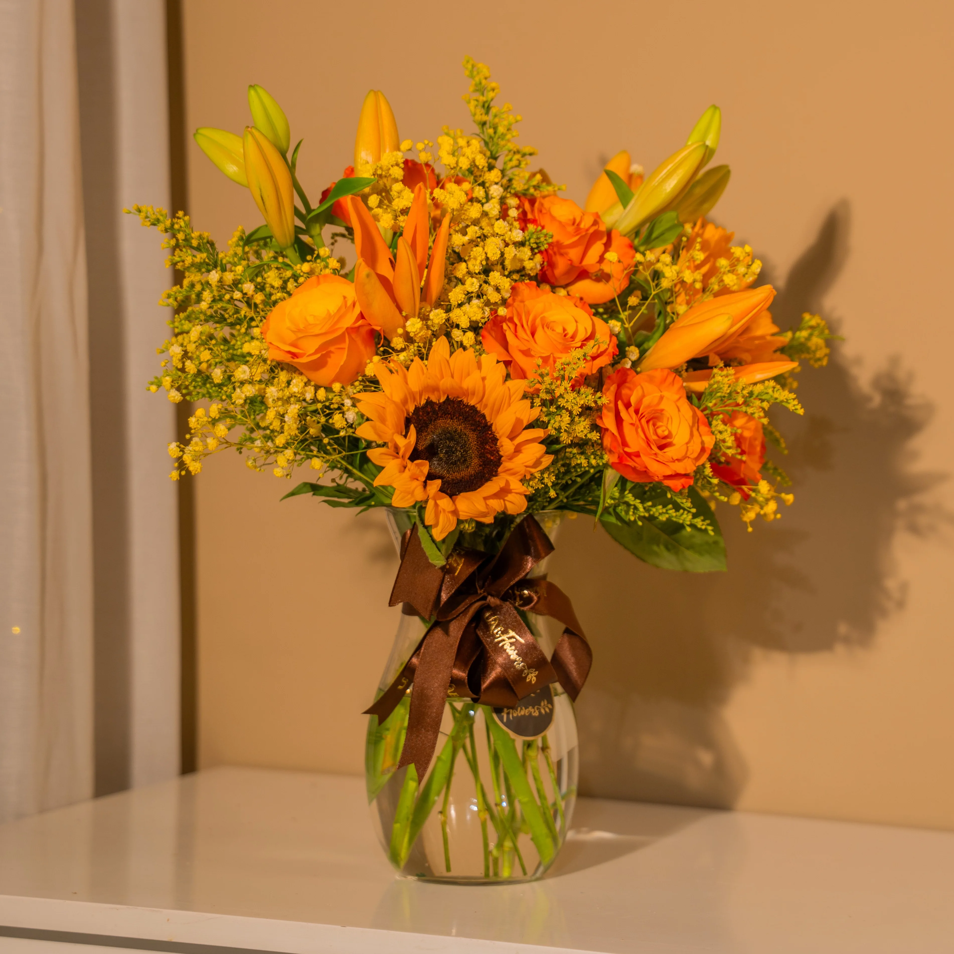 Sunflowers, orange roses, and lilies in a glass vase for Diwali by UAE Flowers Dubai