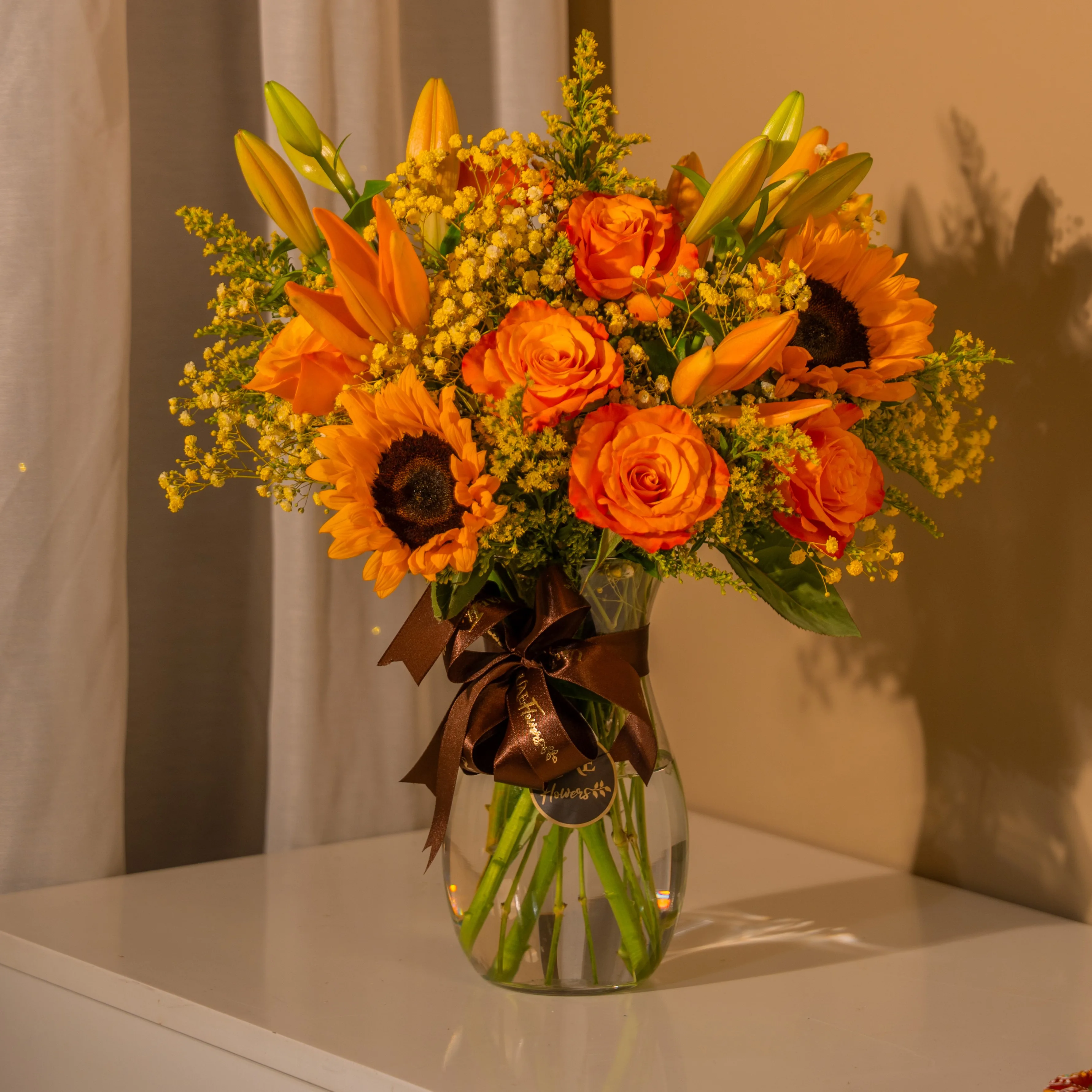 Sunflowers, orange roses, and lilies in a glass vase for Diwali by UAE Flowers Dubai