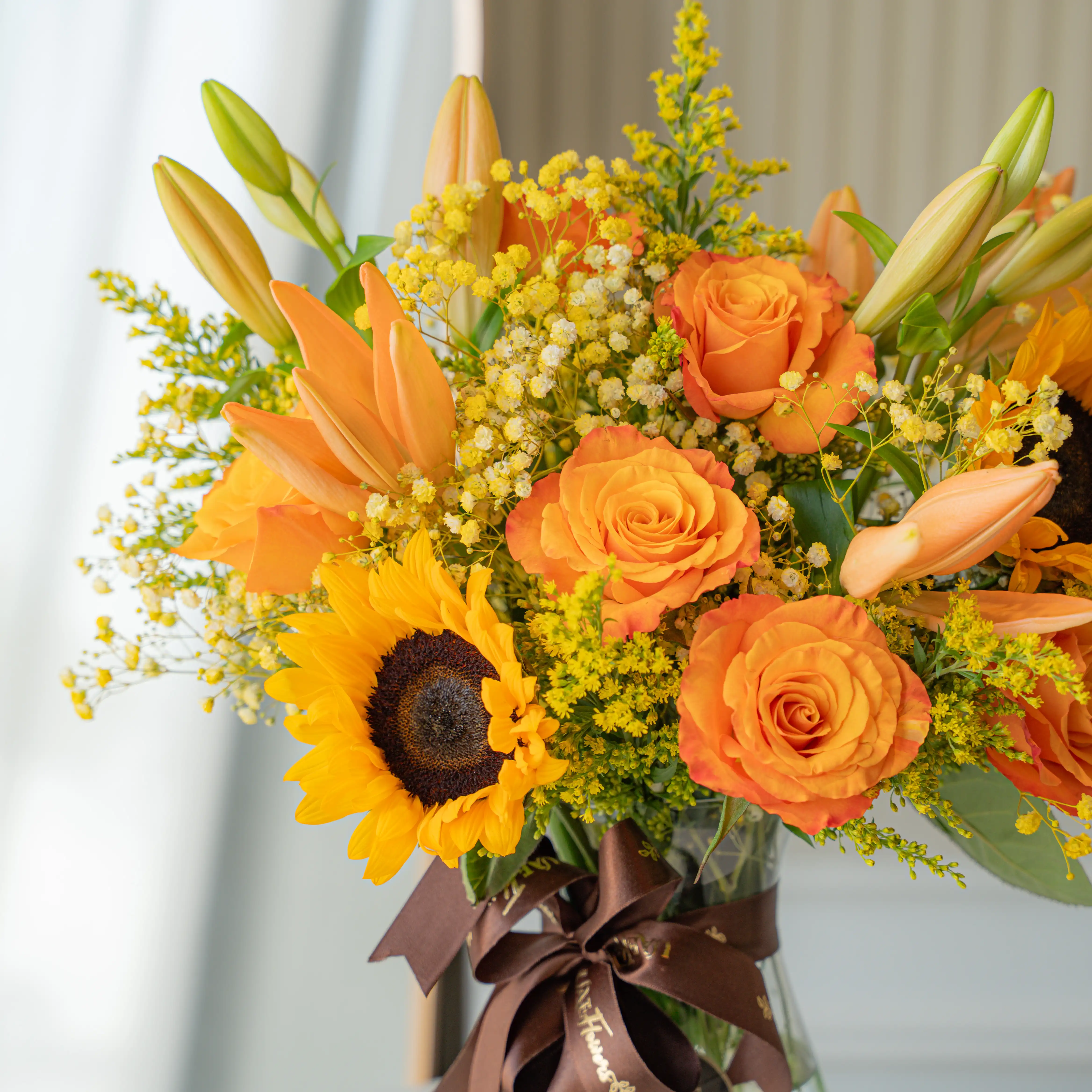 Sunflowers, orange roses, and lilies in a glass vase for Diwali by UAE Flowers Dubai