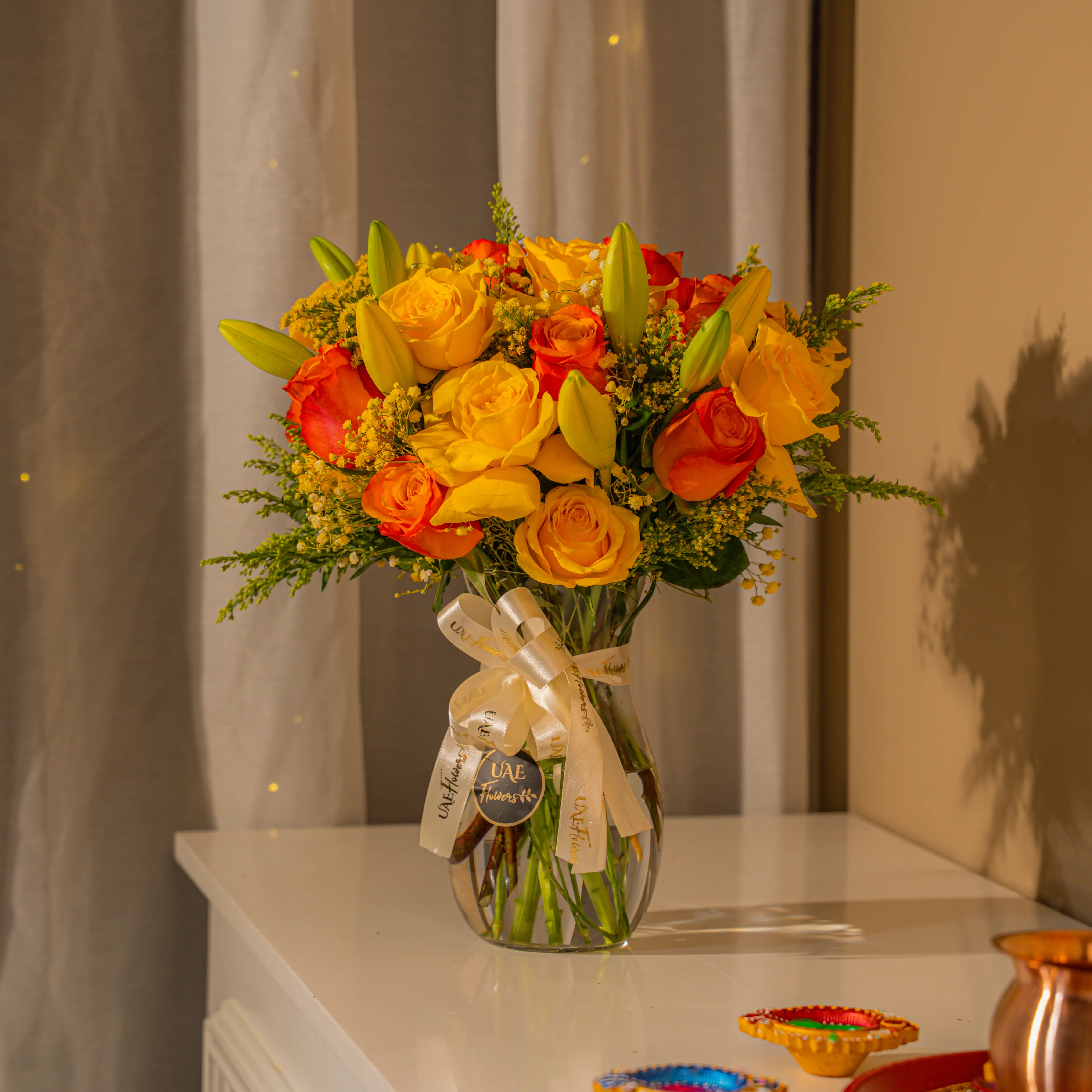 Yellow and orange roses with lilies in glass vase for Diwali by UAE Flowers Dubai