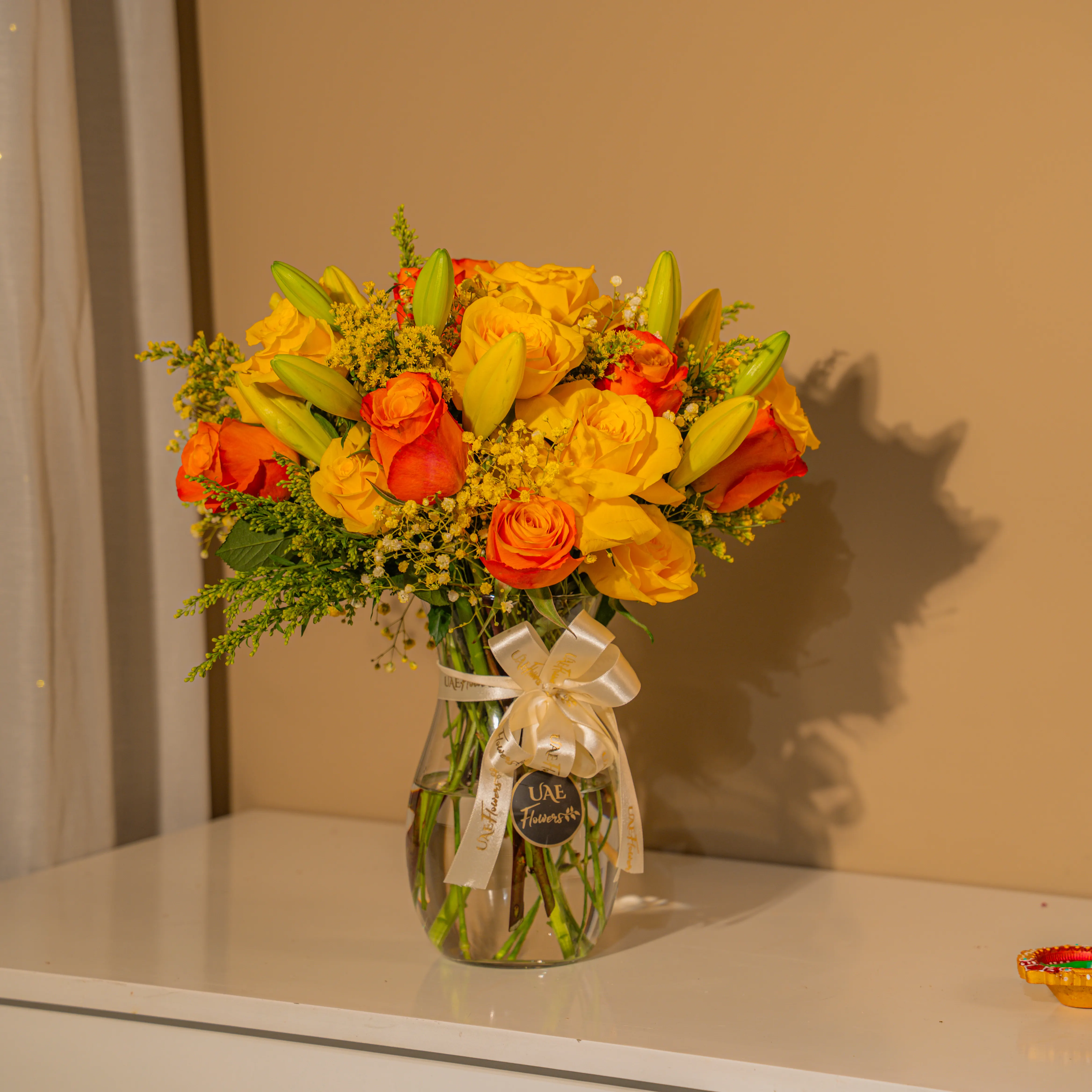Yellow and orange roses with lilies in glass vase for Diwali by UAE Flowers Dubai