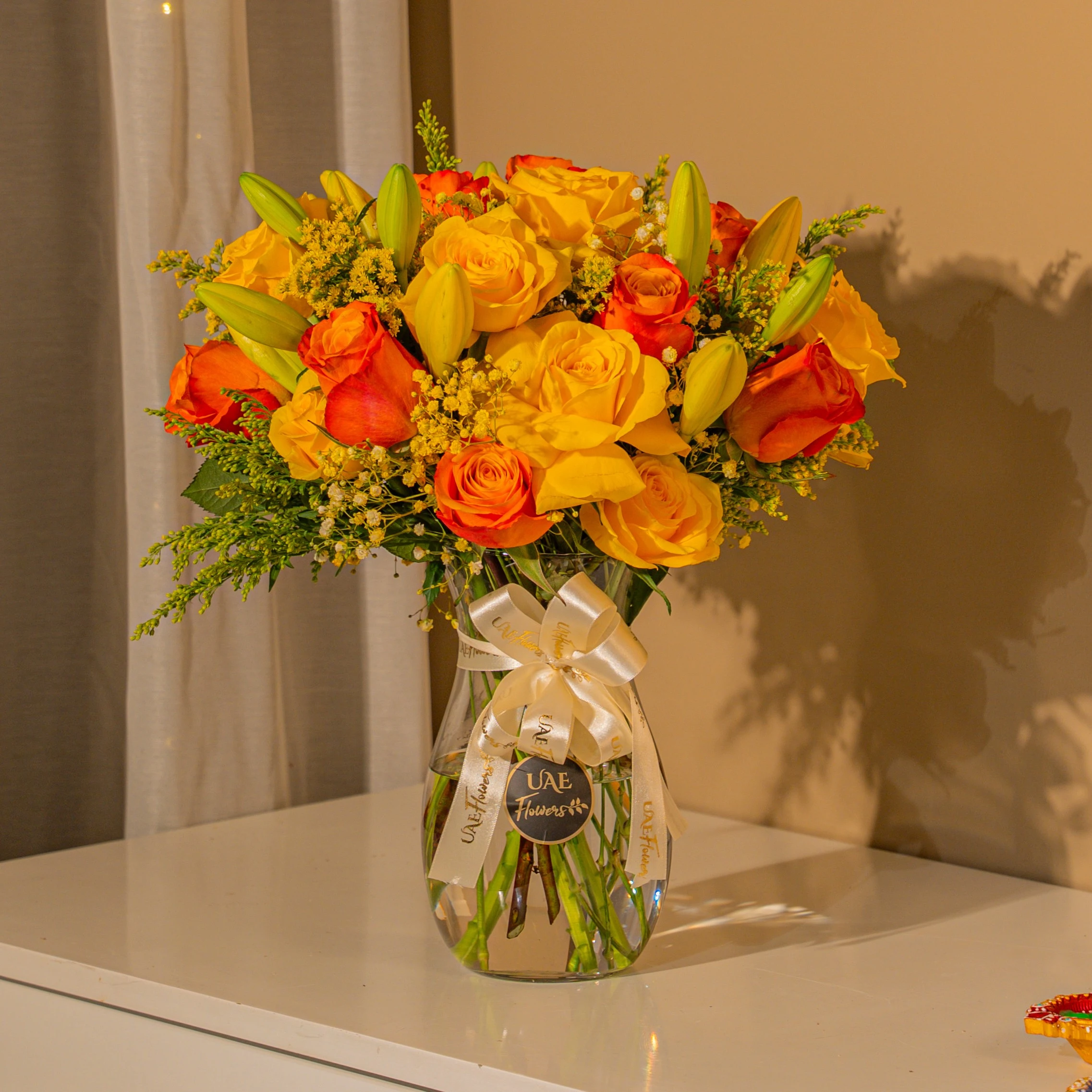 Yellow and orange roses with lilies in glass vase for Diwali by UAE Flowers Dubai