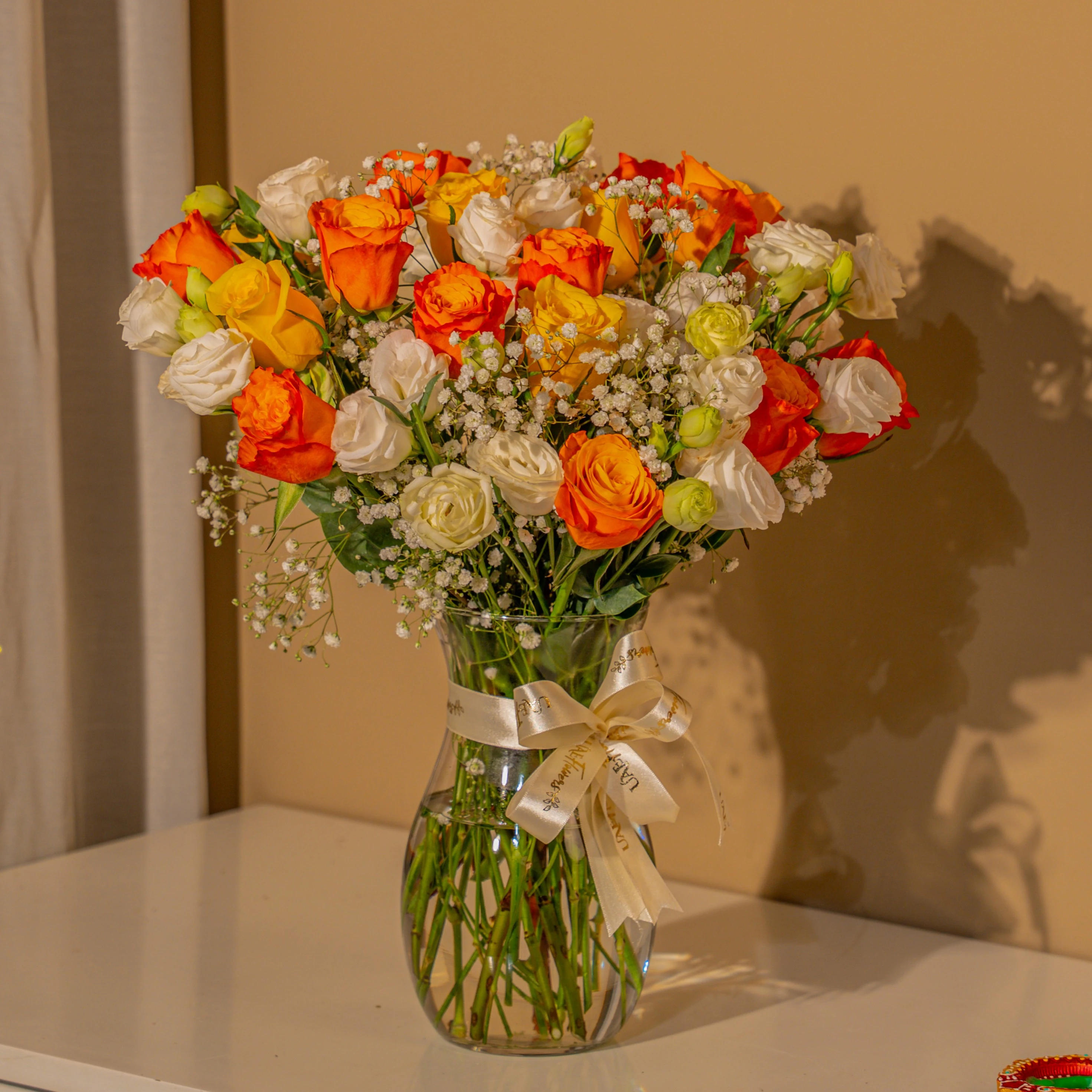 Orange, yellow, and white roses in glass vase for Diwali by UAE Flowers Dubai