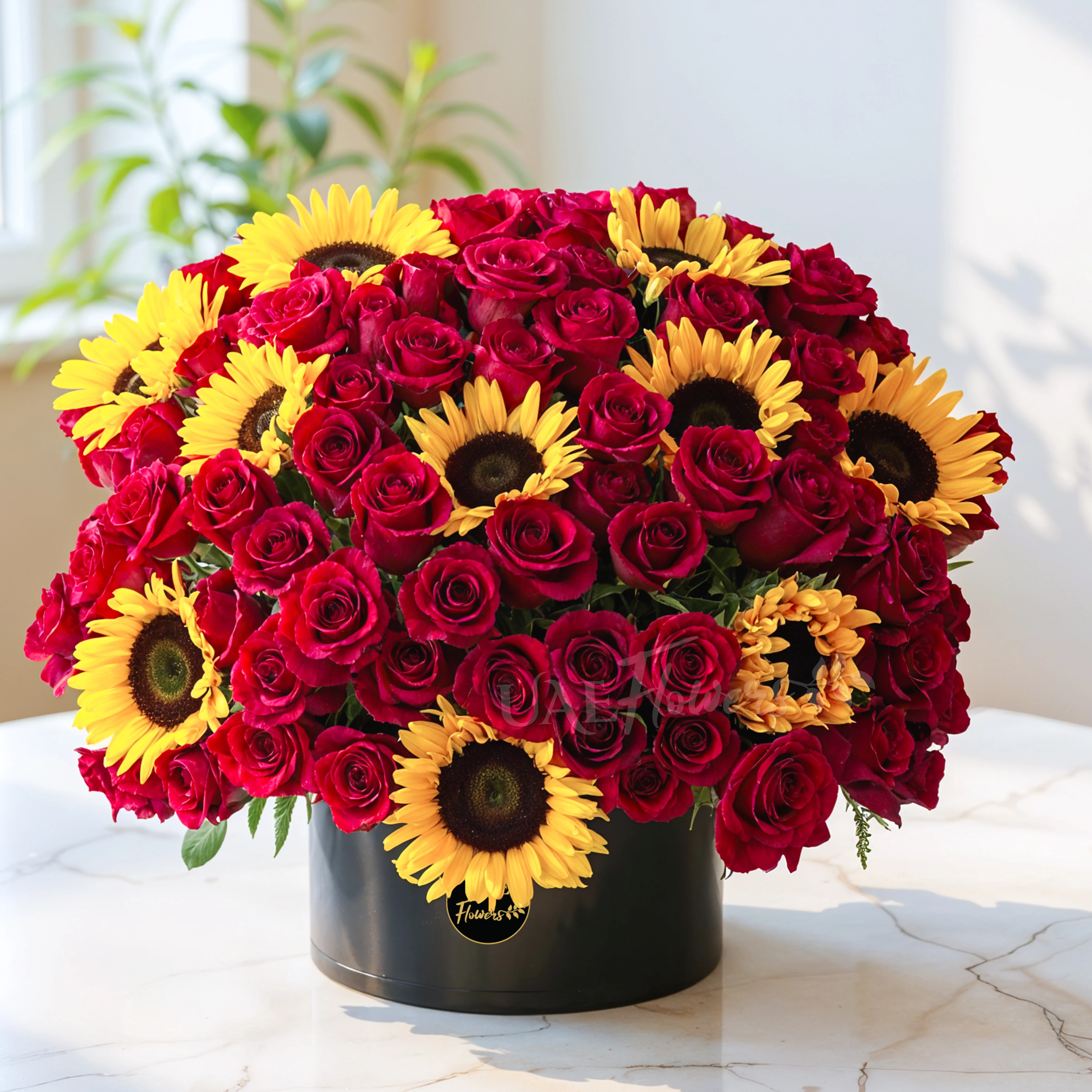 One side round arrangement of 10 sunflowers and 60 red roses with greens in a black round box.