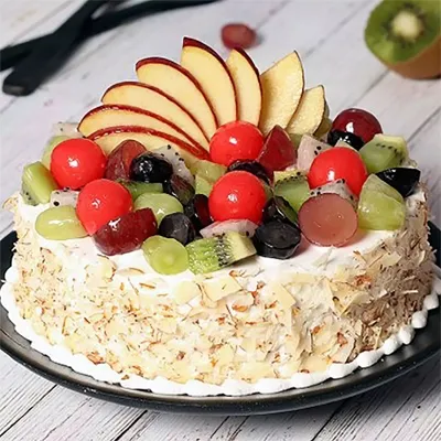 A 1 kg of vanilla sponge fruit cake topped with vanilla cream, mixed fruits, and sides decorated with sliced almonds